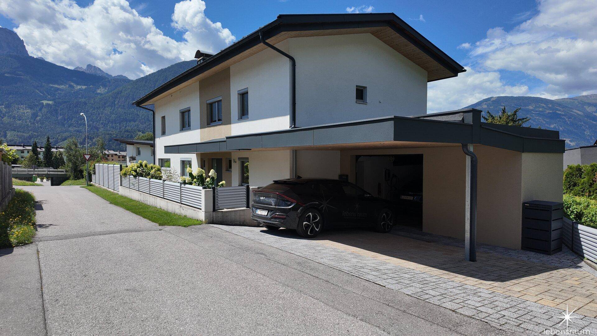 Einfamilienhaus mit Carport, gepflasterter Auffahrt und Bergblick.