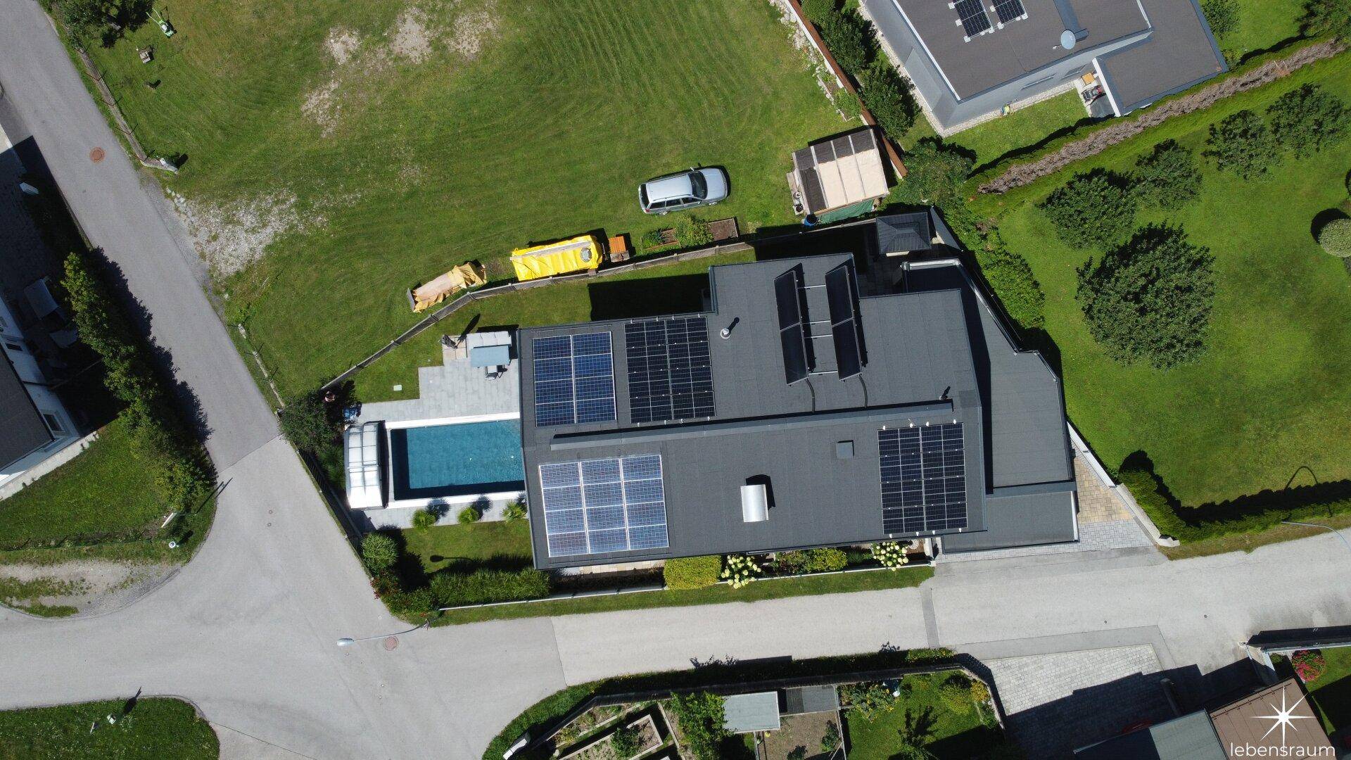Luftaufnahme eines modernen Hauses mit Flachdach, Solaranlagen und einem Außenpool im Gartenbereich.
