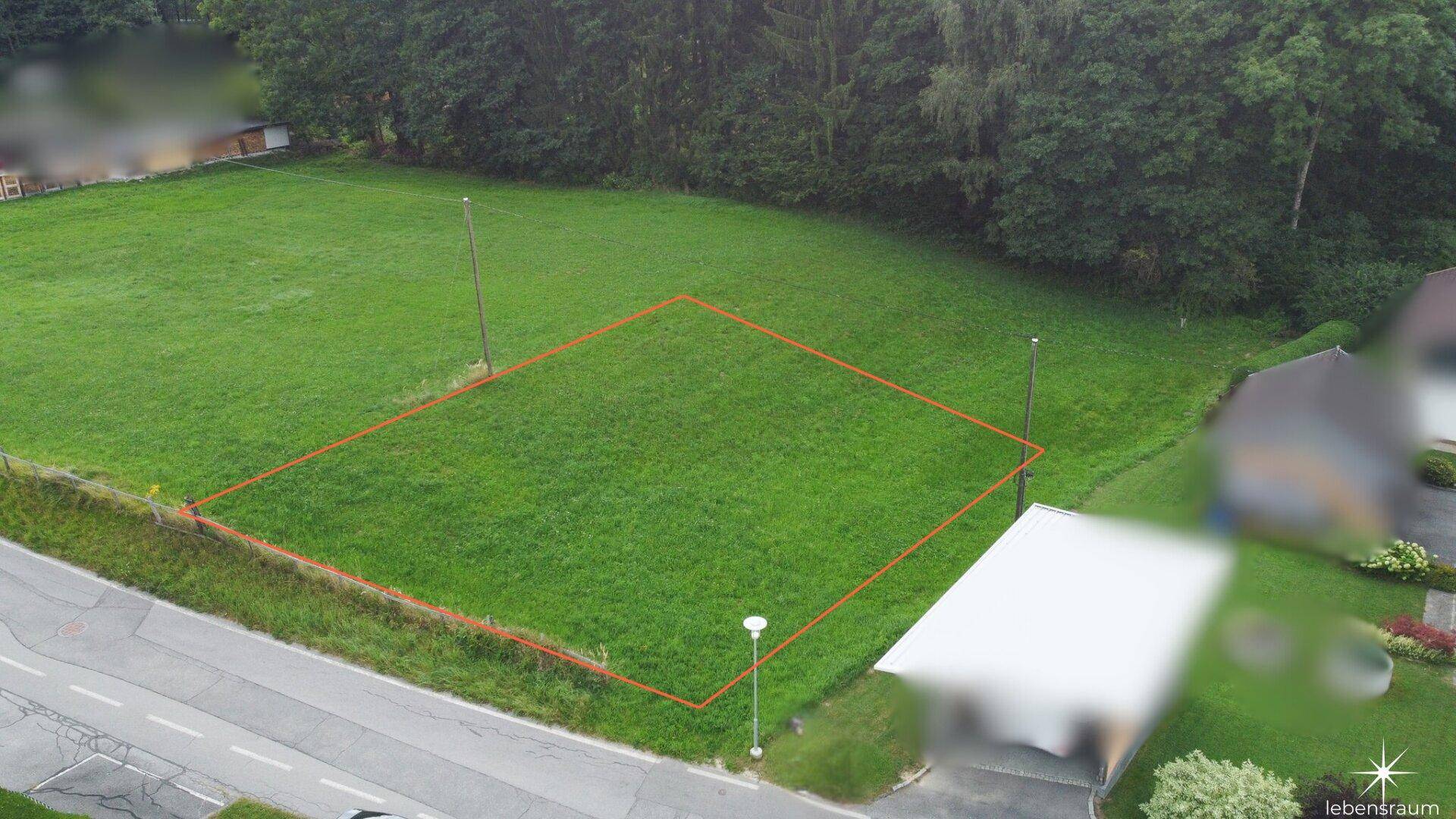 Weitläufige Luftaufnahme eines grünen Baugrundstücks, umgeben von Bäumen und einer Straße.