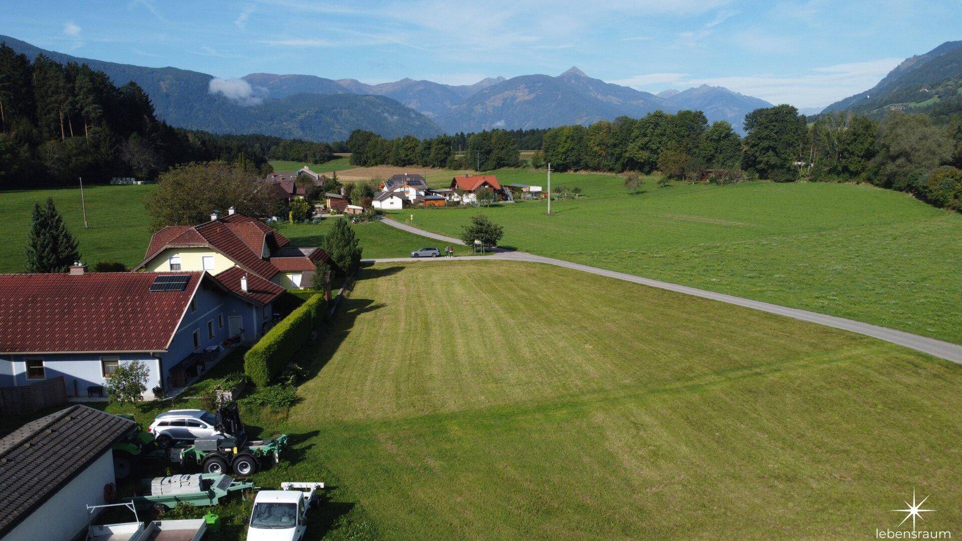 Weitläufige Luftaufnahme eines grünen Grundstücks mit umliegenden Häusern und beeindruckendem Bergblick.