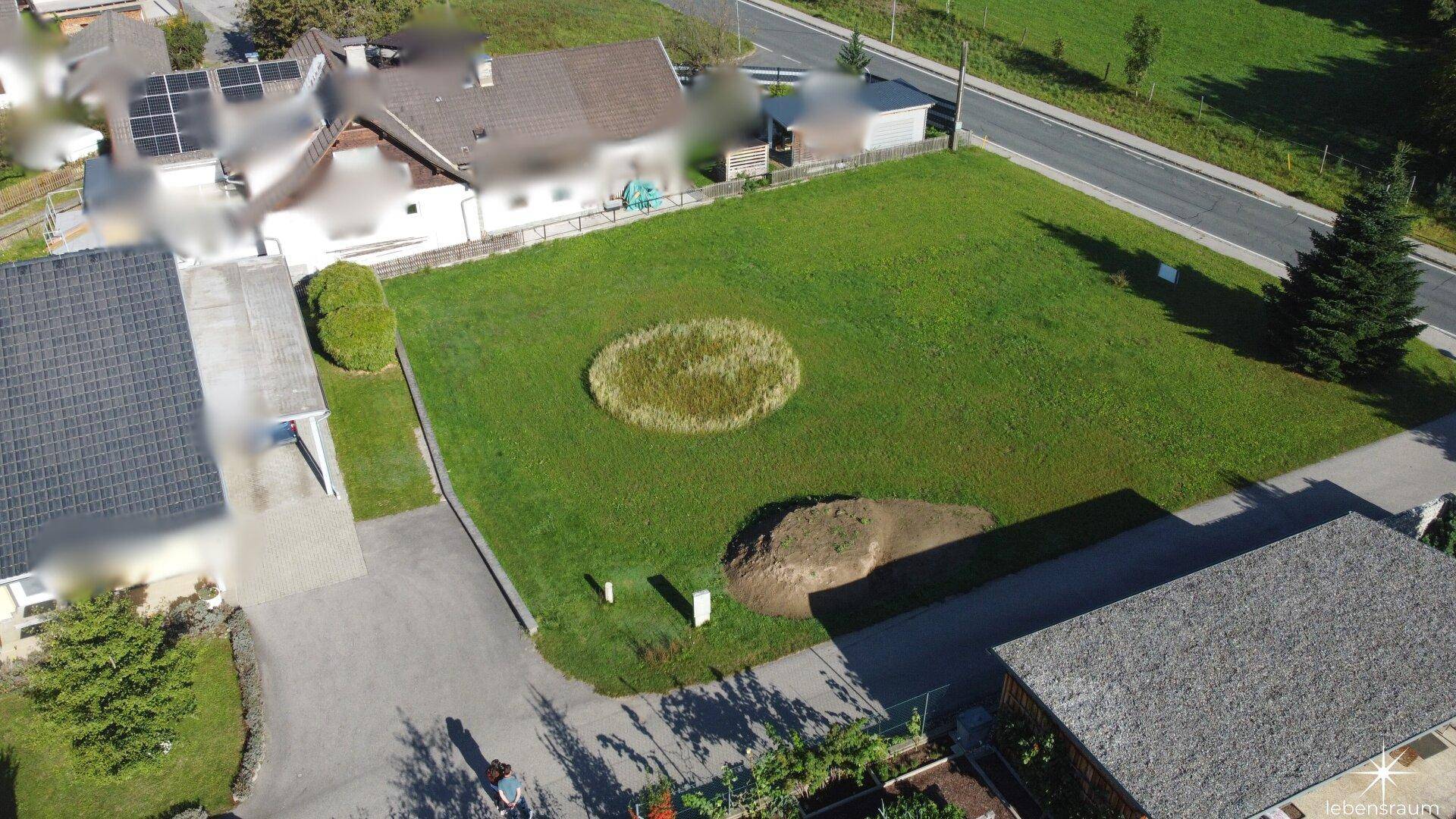 Übersicht des grünen Baugrundstücks mit angrenzenden Häusern und Zufahrtswegen.