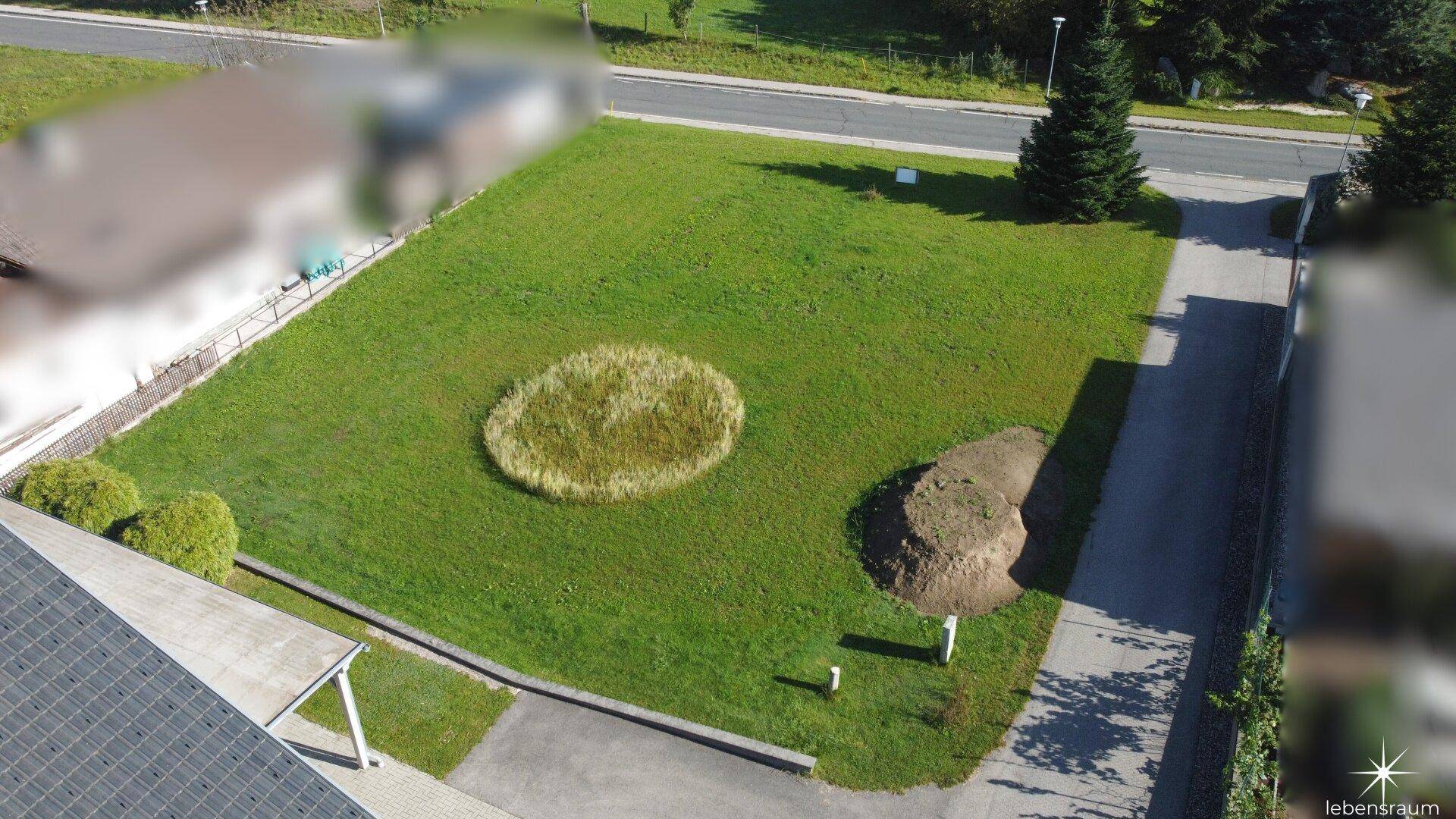 Detailansicht des Baugrundstücks mit Rasenfläche und angrenzenden Wegen.