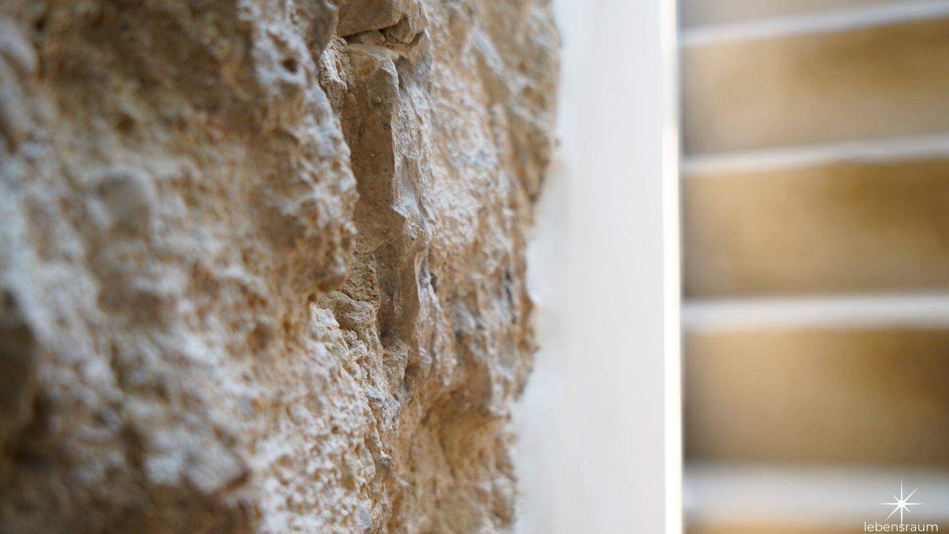 Nahaufnahme einer rustikalen Steinwand neben einer Treppe, die den Charakter des Hauses betont.