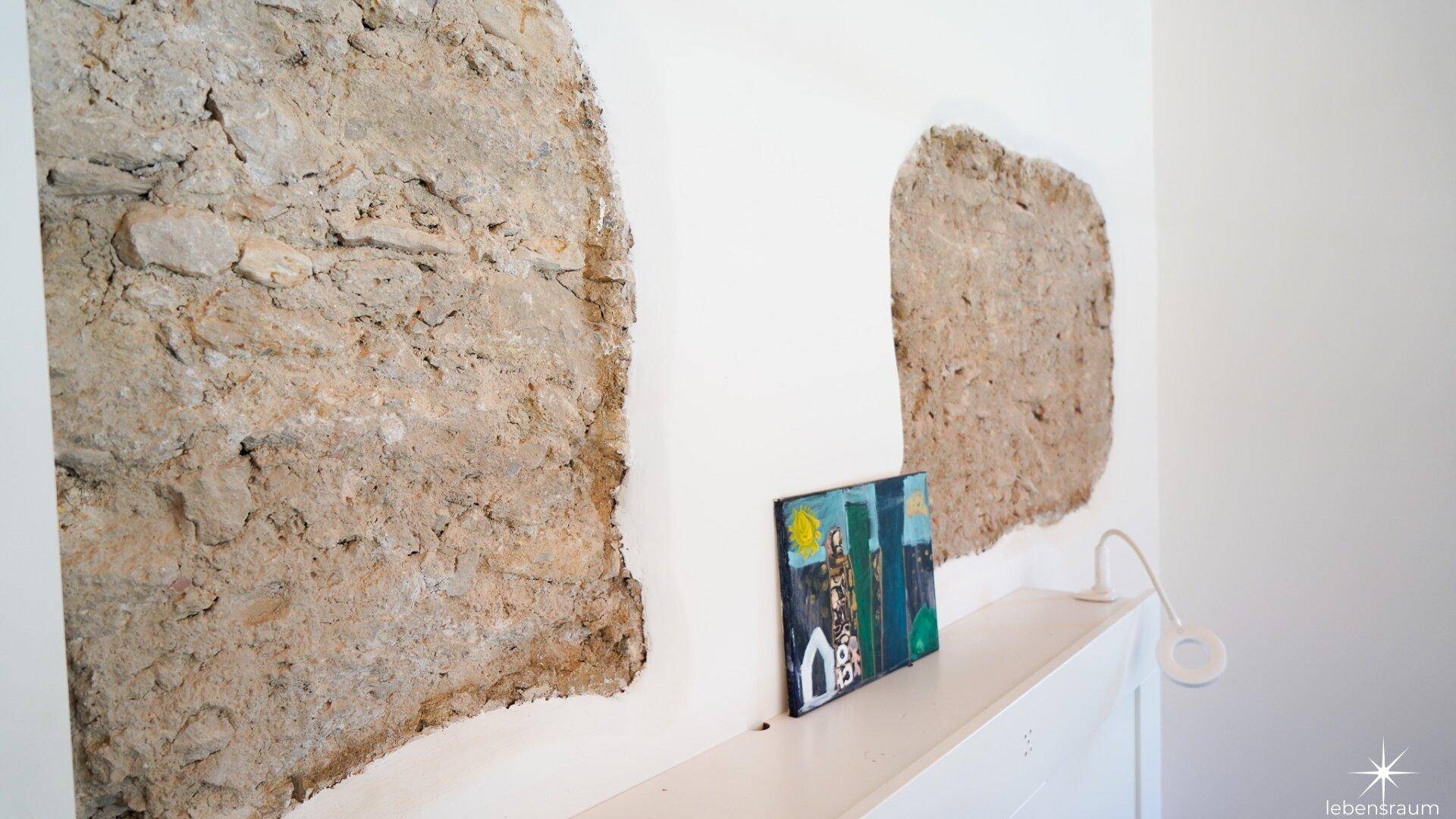 Detailaufnahme einer Wand mit freigelegten Steinabschnitten und einem kleinen Kunstwerk.