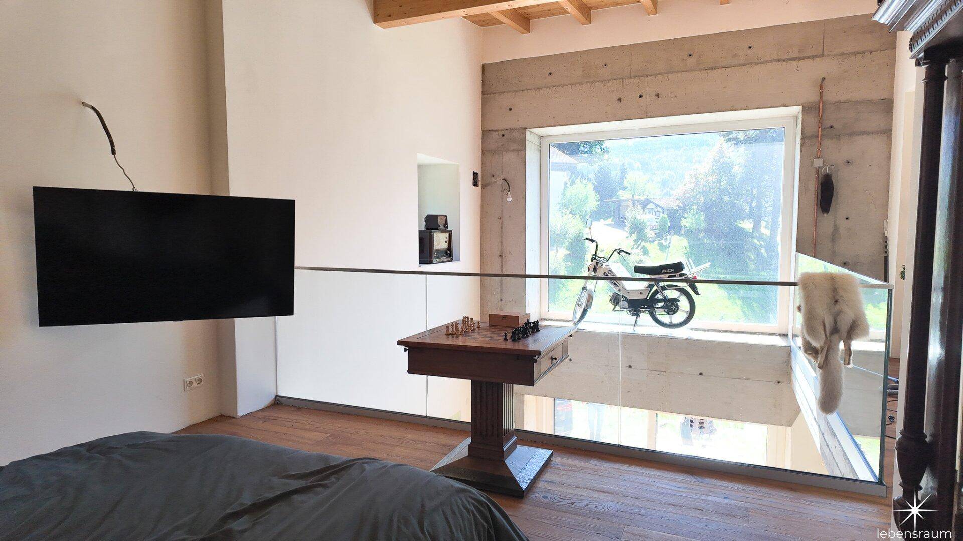 Schlafzimmer auf einer Galerie mit großem Fenster und Blick auf die Umgebung.