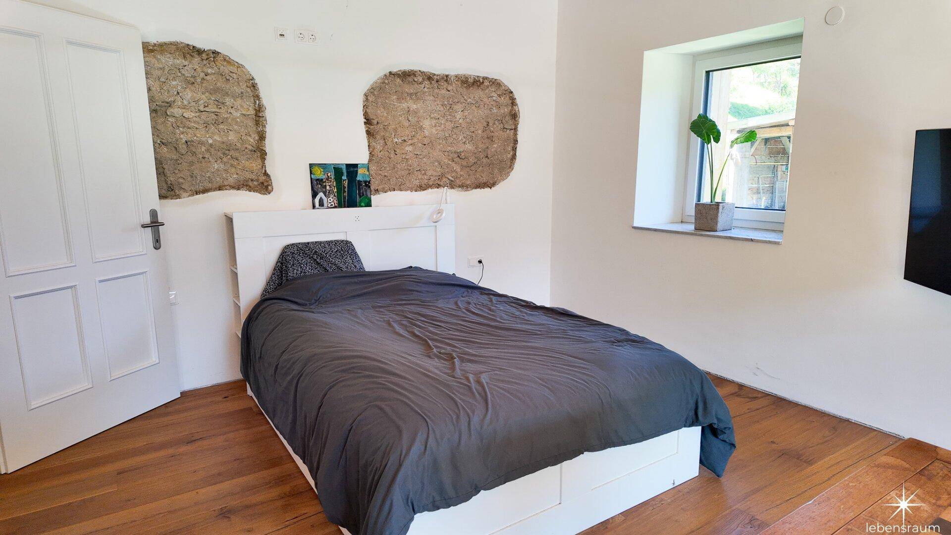 Schlafzimmer mit Holzboden, weißem Bett und charakteristischen freigelegten Steinwänden.