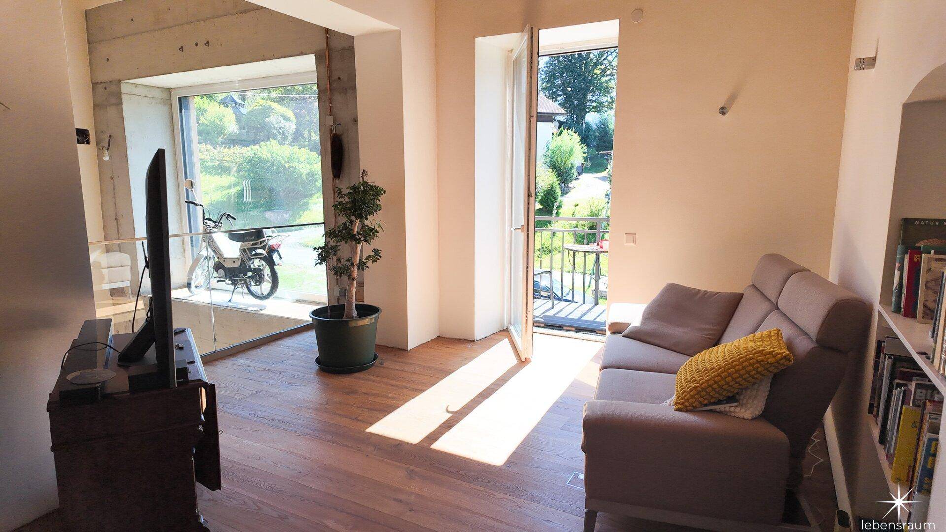 Helles Wohnzimmer mit Holzboden, Sofa und Zugang zu einem kleinen Balkon.