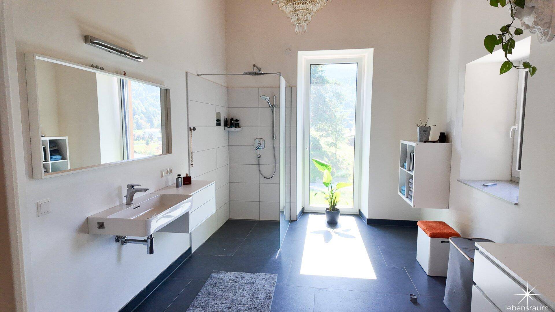 Großes, helles Badezimmer mit bodentiefen Fenstern, Dusche und modernem Waschtisch.