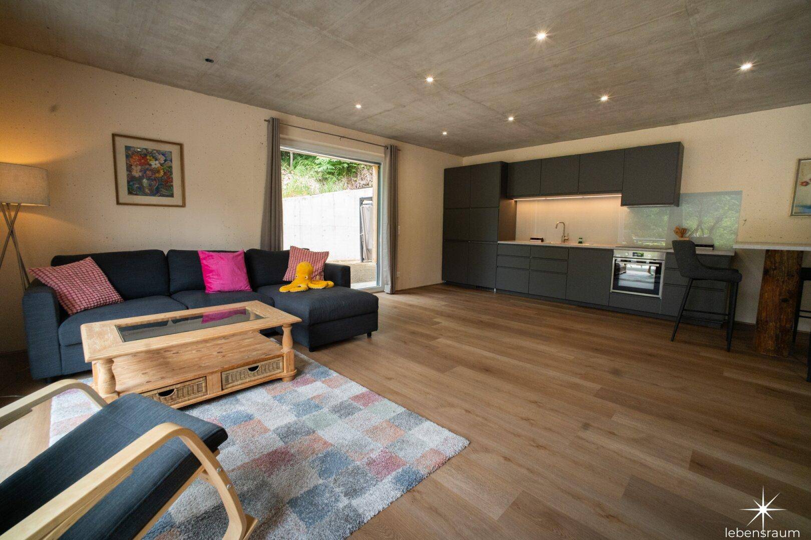 Offener Wohnbereich mit integrierter Küchenzeile, Holzboden und Terrassenzugang.