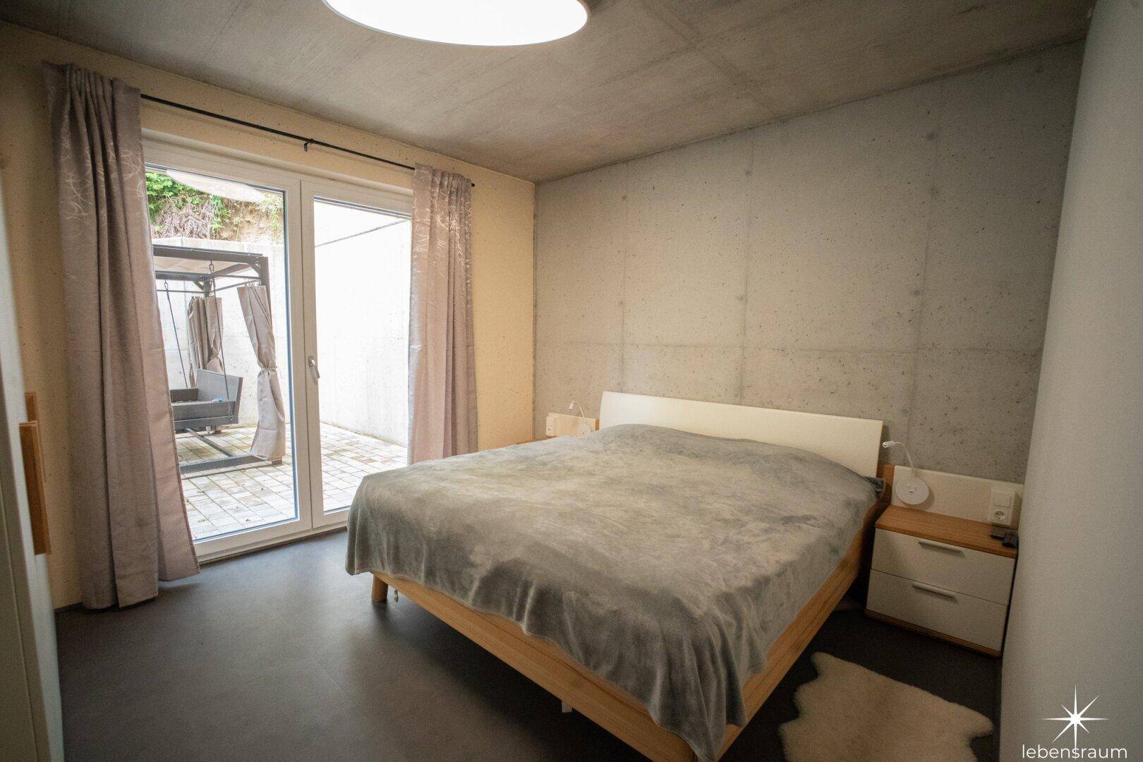 Schlafzimmer mit Holzbett, dunklem Boden und Zugang zu einem kleinen Außenbereich.