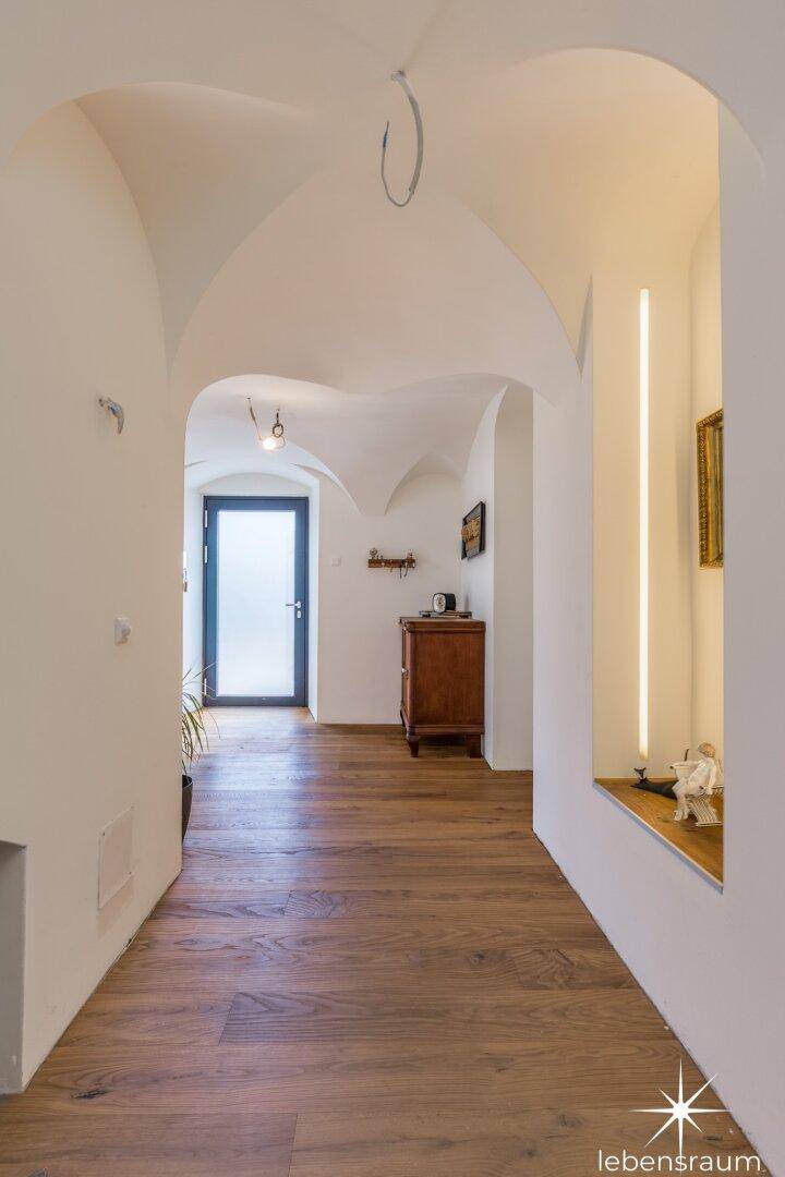 Langer Flur mit Holzboden, eleganten Gewölbedecken und moderner Beleuchtung.