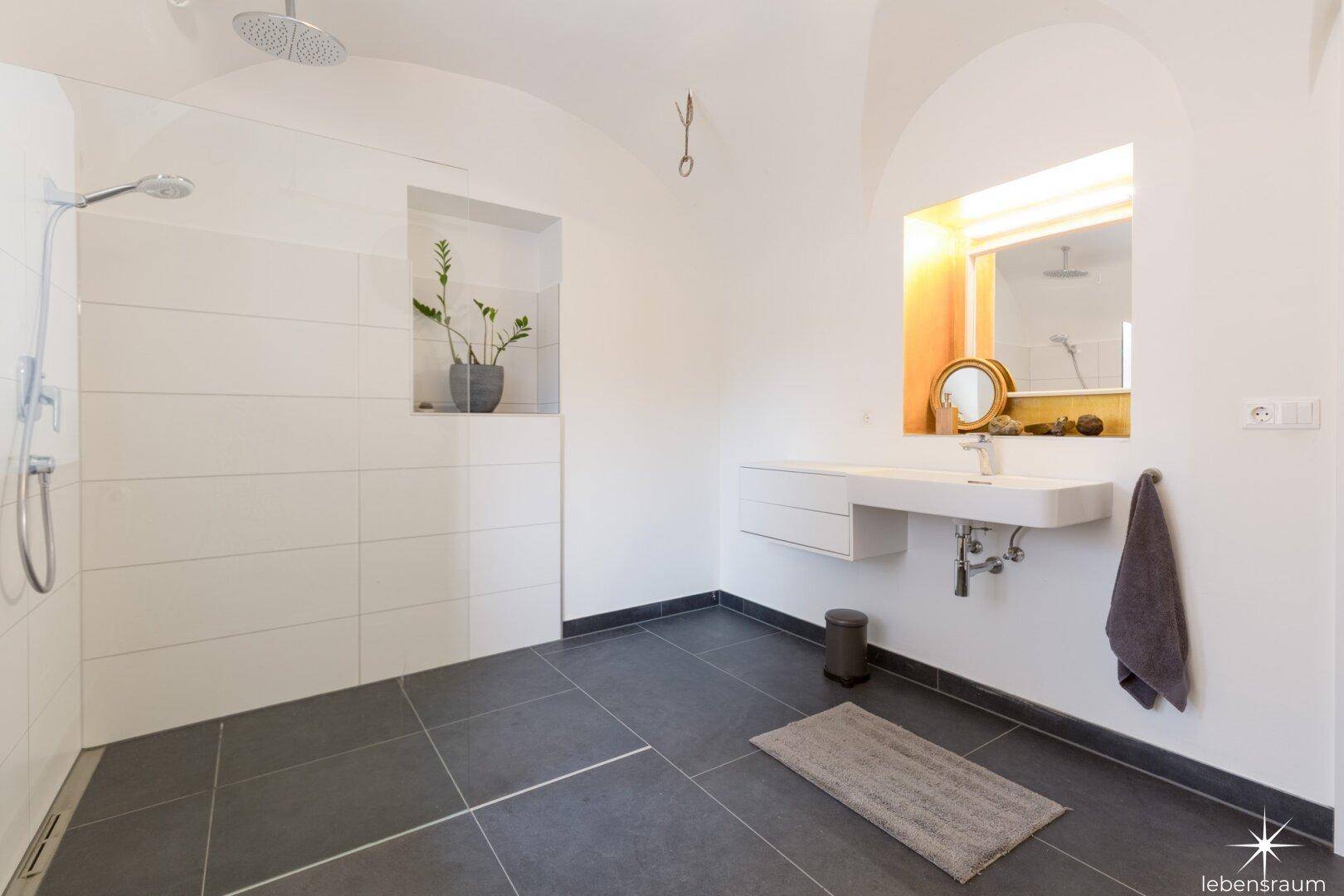 Modernes Badezimmer mit dunklen Fliesen, begehbarer Dusche und schwebendem Waschtisch.