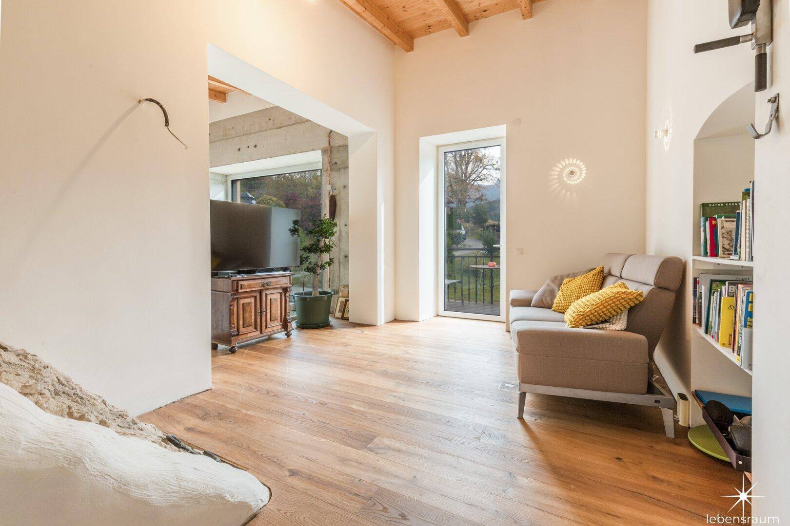 Heller Wohnbereich mit Holzboden, Sofa und Blick ins Grüne.