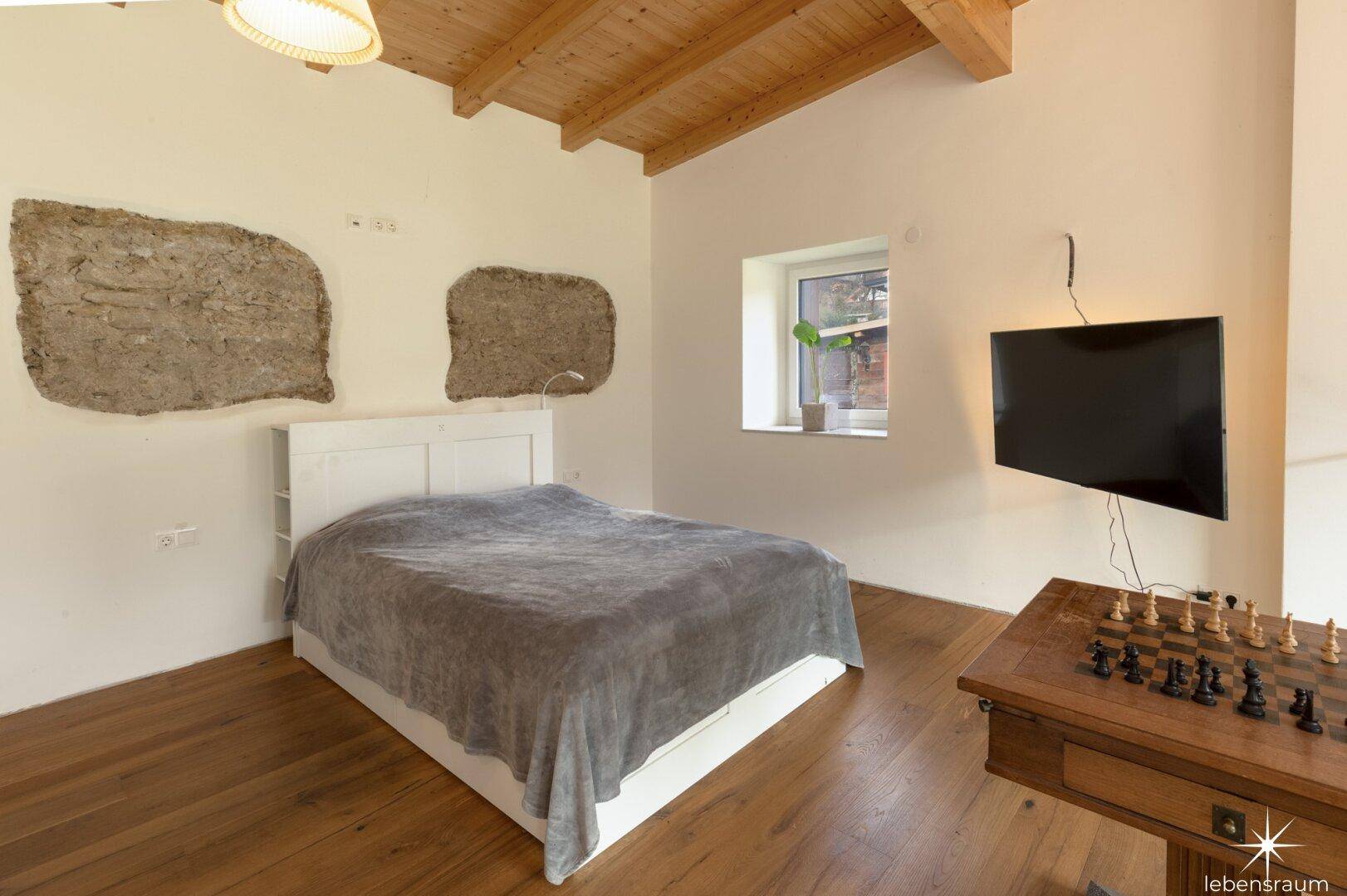 Schlafzimmer mit Holzboden, Bett und freigelegten Steinwänden.