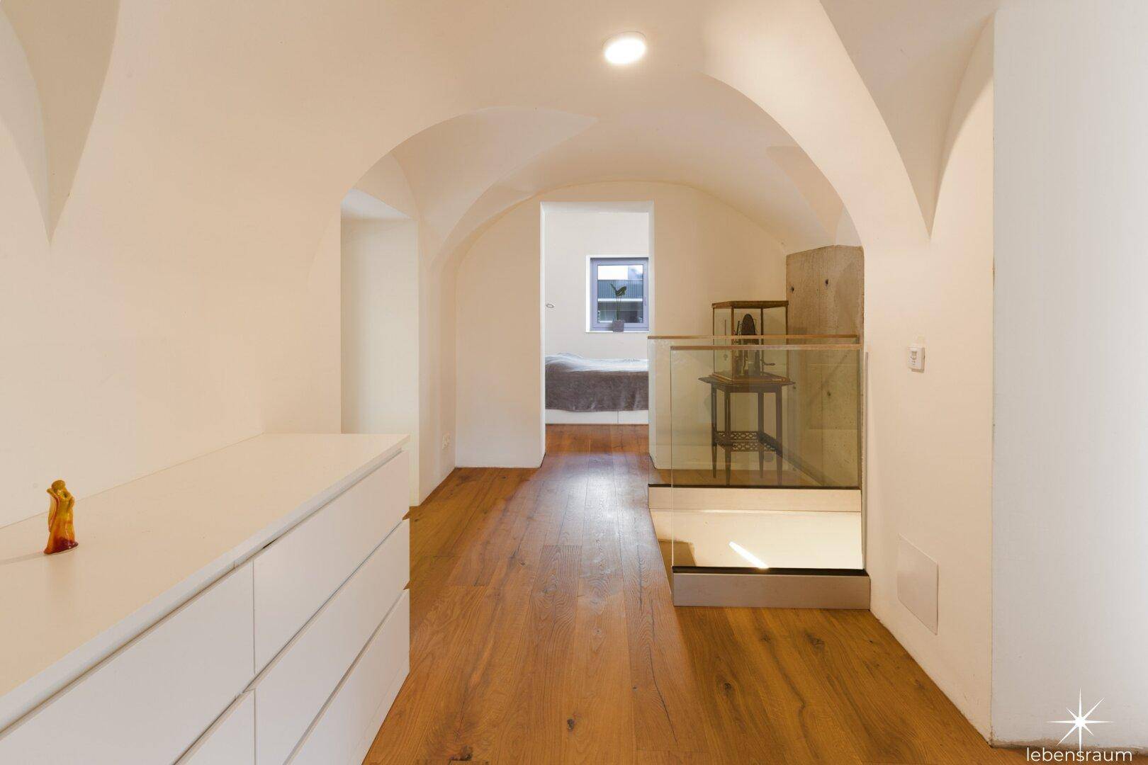 Flur mit Holzboden, Gewölbedecken und Blick in ein Schlafzimmer.