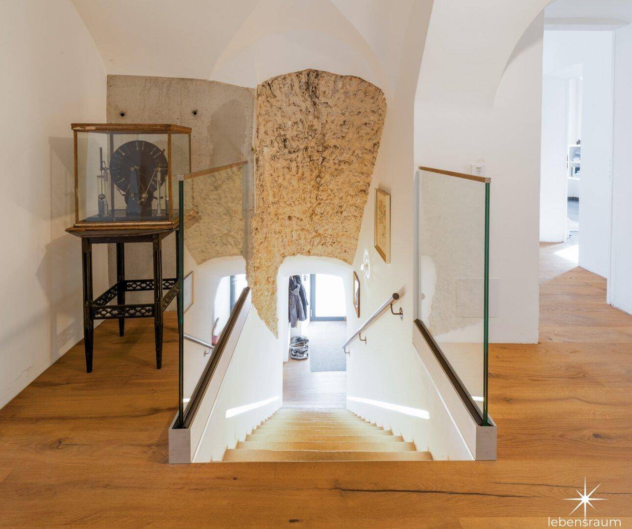Treppenabgang mit Glasgeländer und freigelegter Steinwand, die den historischen Charakter betont.