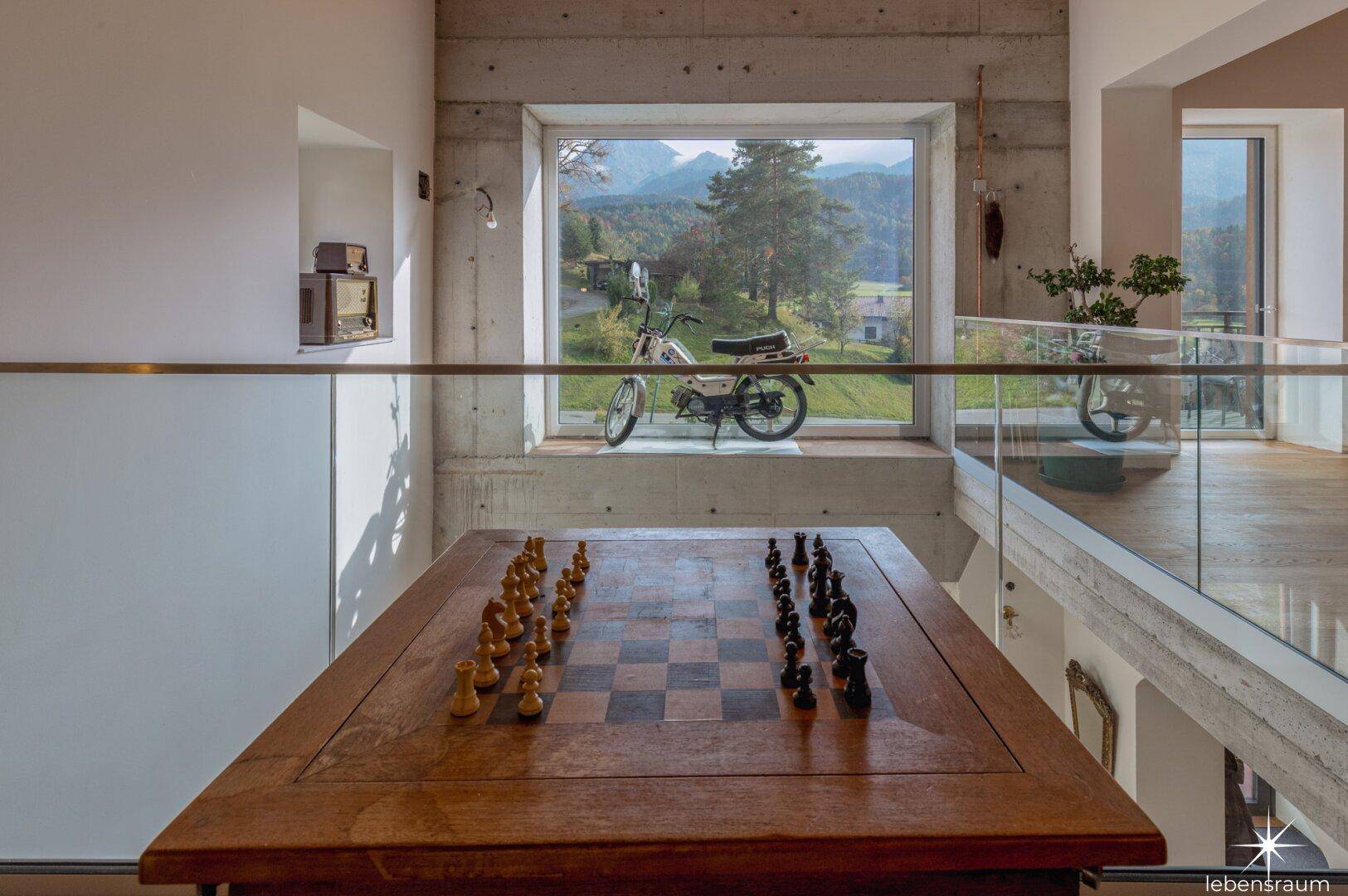 Galeriebereich mit Schachspiel, großem Fenster und beeindruckendem Bergblick.