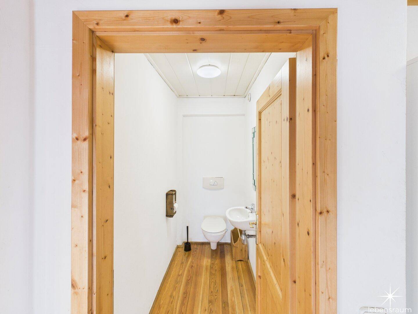 Kleines Gäste-WC mit Holzvertäfelung, weißer Toilette und Waschbecken, funktional und hell.