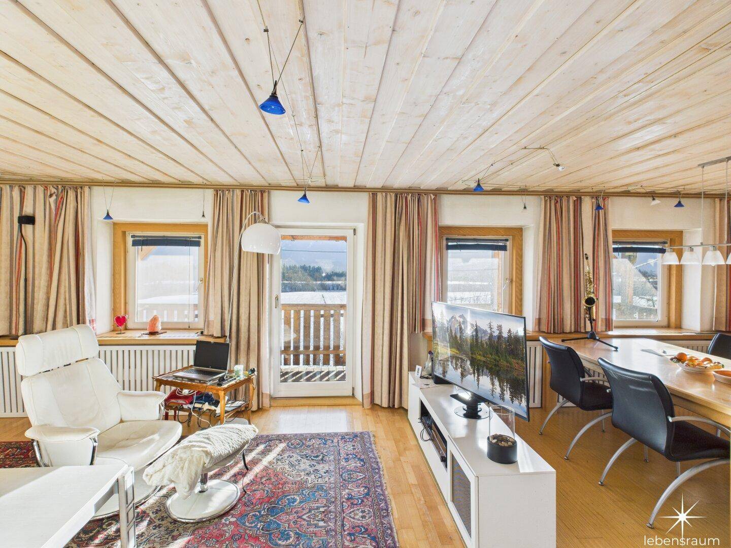 Heller Wohnbereich mit Balkonzugang, Holzbalkendecke und Blick auf die Landschaft, gemütlich eingerichtet.