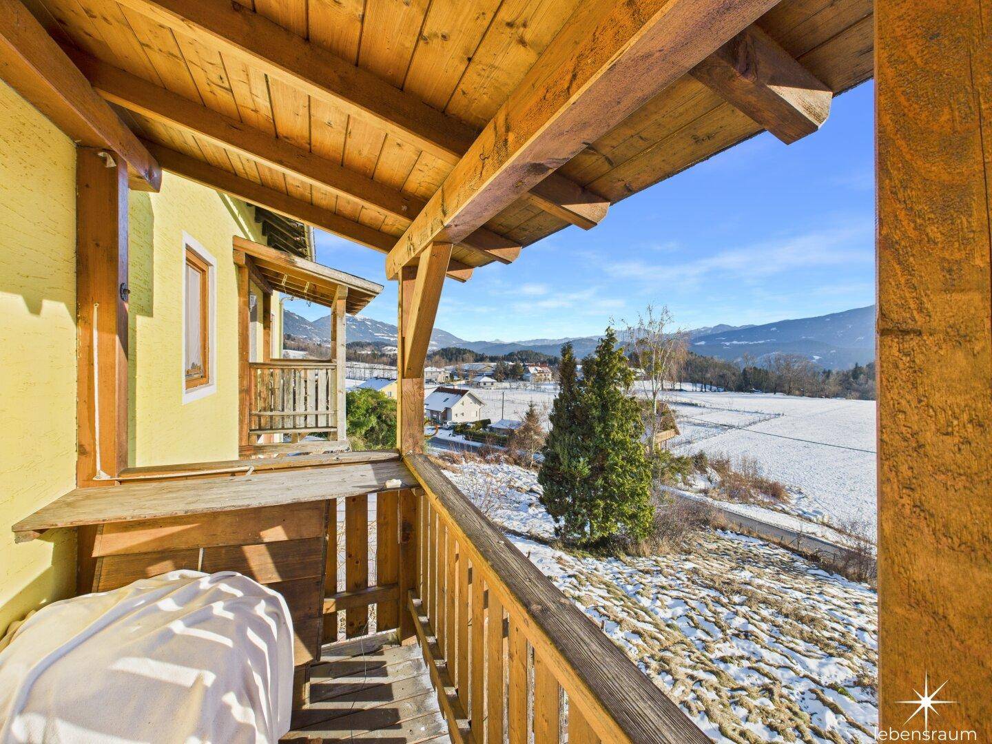 Überdachter Holzbalkon mit Blick auf die verschneite Landschaft und die Berge, ideal für frische Luft.