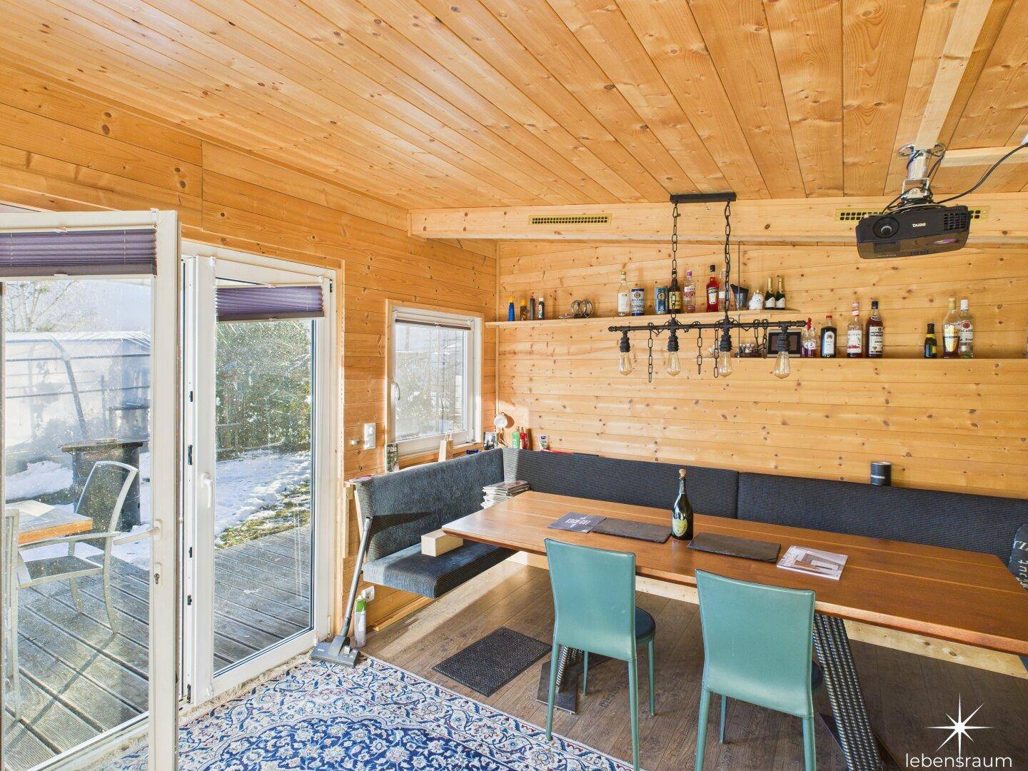 Gemütlicher Essbereich in einem Holzhaus mit langer Sitzbank und Terrassenzugang, rustikal und einladend.