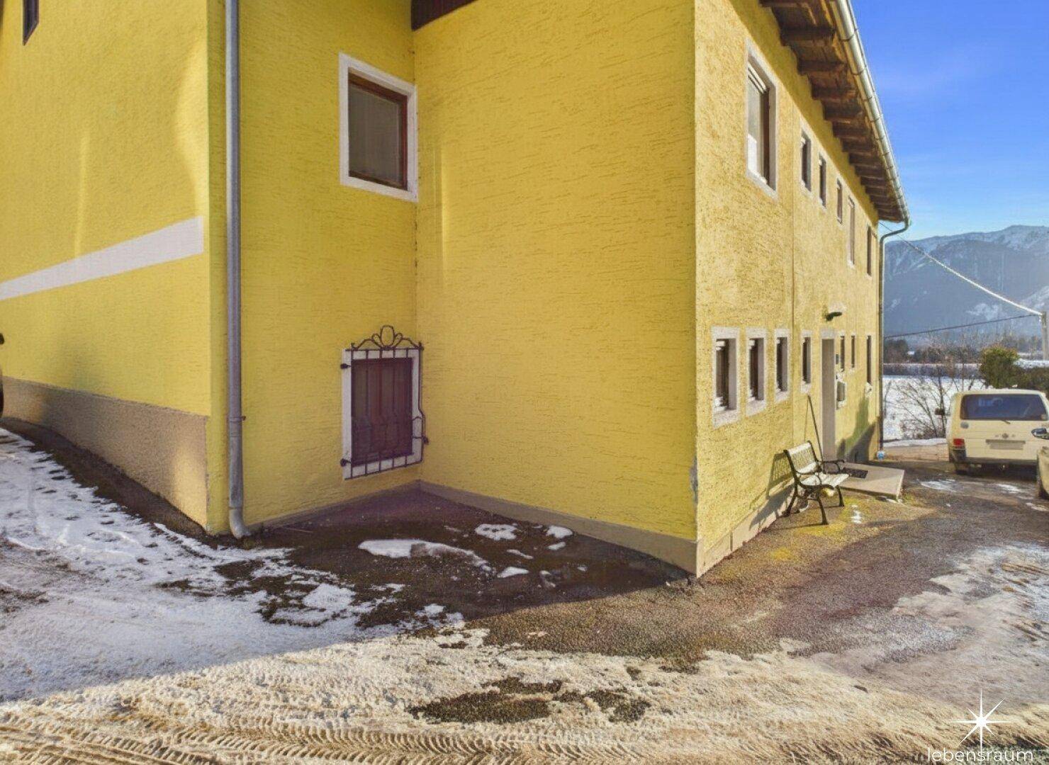 Seitenansicht des gelben Gebäudes mit kleinen Fenstern und verschneitem Vorplatz, traditioneller Stil.