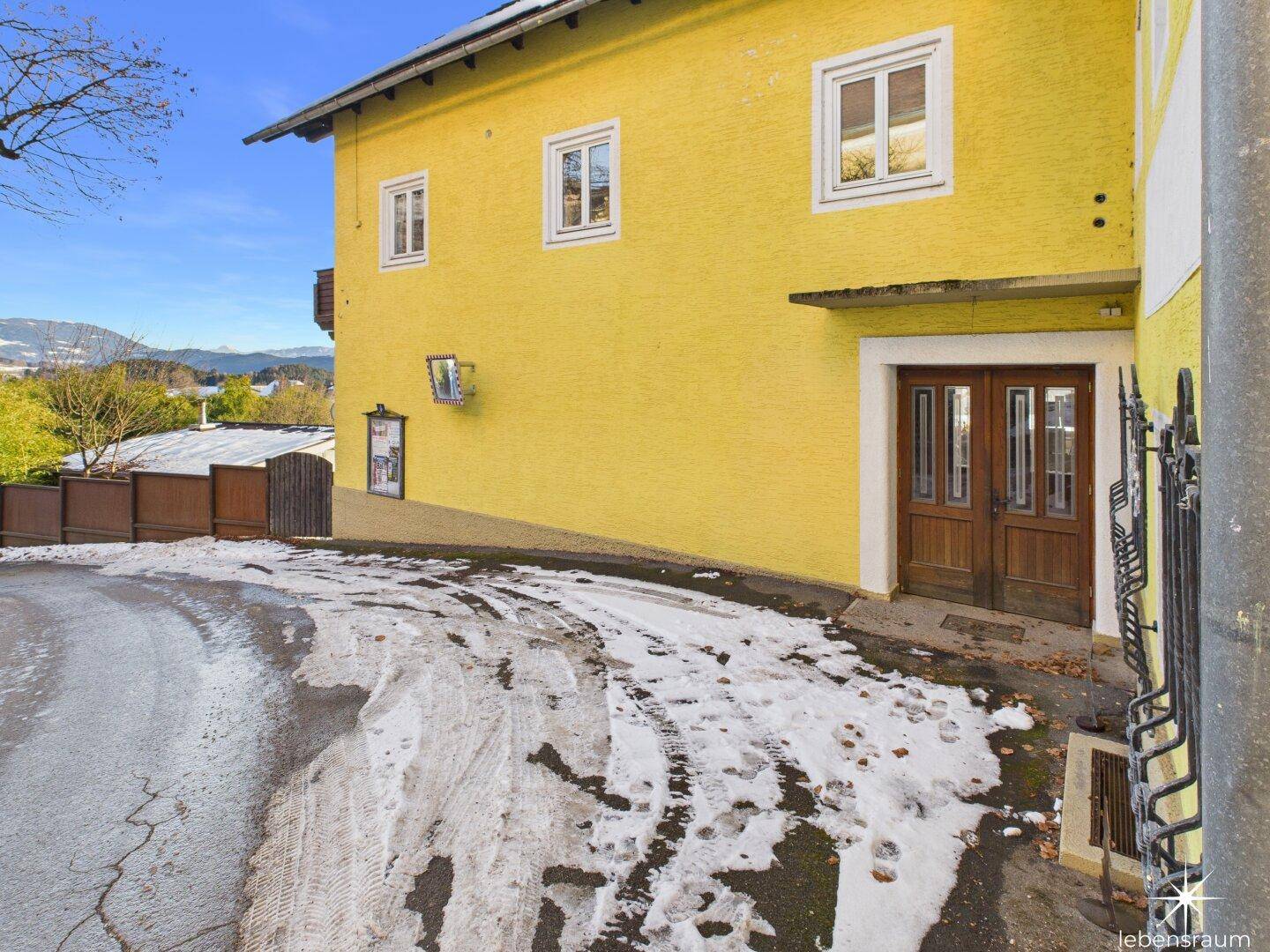 Haupteingang des gelben Gebäudes mit Holztüren und verschneiter Auffahrt, einladend und rustikal.