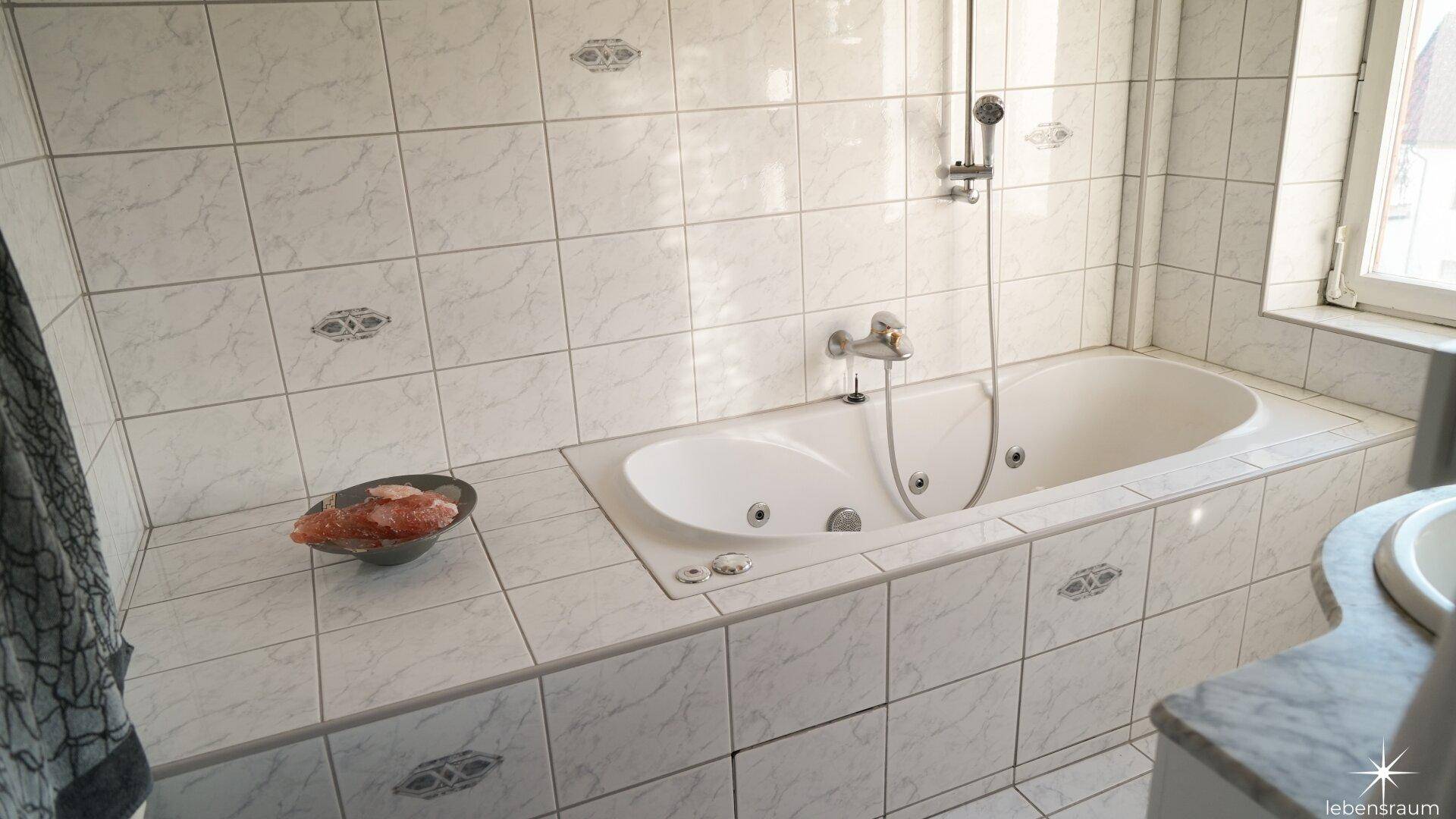 Badezimmer mit Whirlpool-Badewanne, weißen Fliesen und kleinem Fenster, modern und entspannend.
