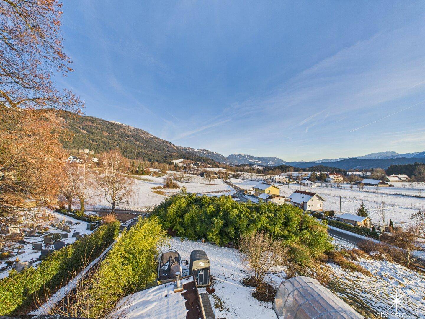 Panoramablick über die verschneite Landschaft mit Bergen und grünen Bäumen unter blauem Himmel.