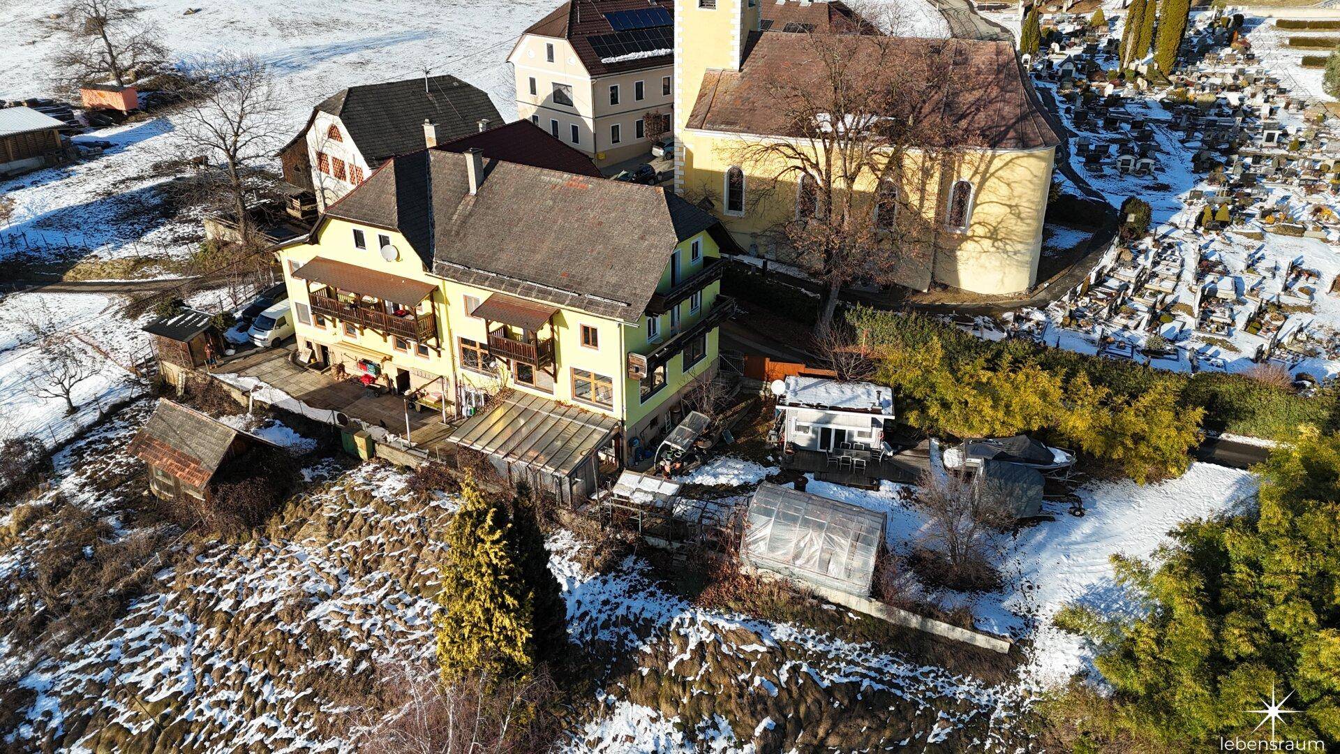 Vogelperspektive des Anwesens mit Kirche, Friedhof und verschneiter Umgebung, malerische Ansicht.