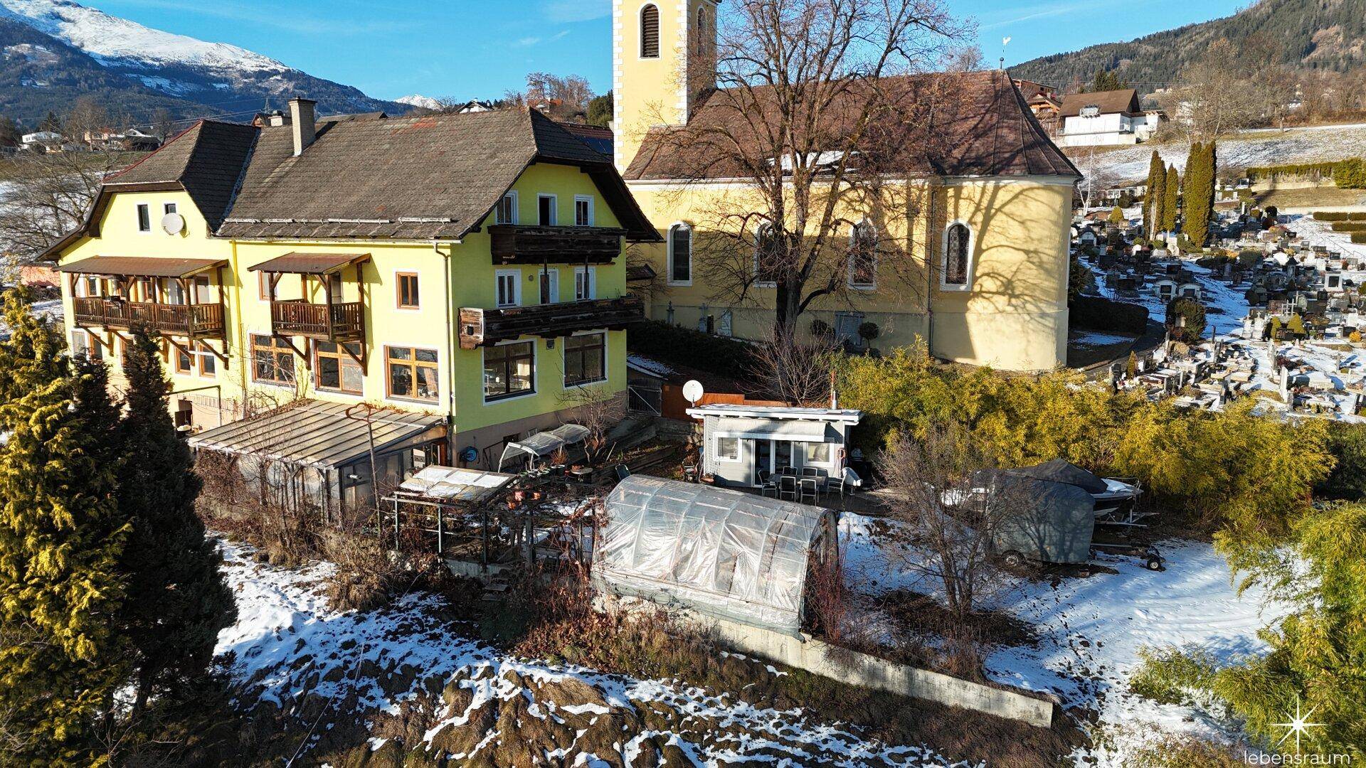 Luftaufnahme des Anwesens mit Kirche, Gewächshäusern und verschneiten Feldern, ländliche Idylle.