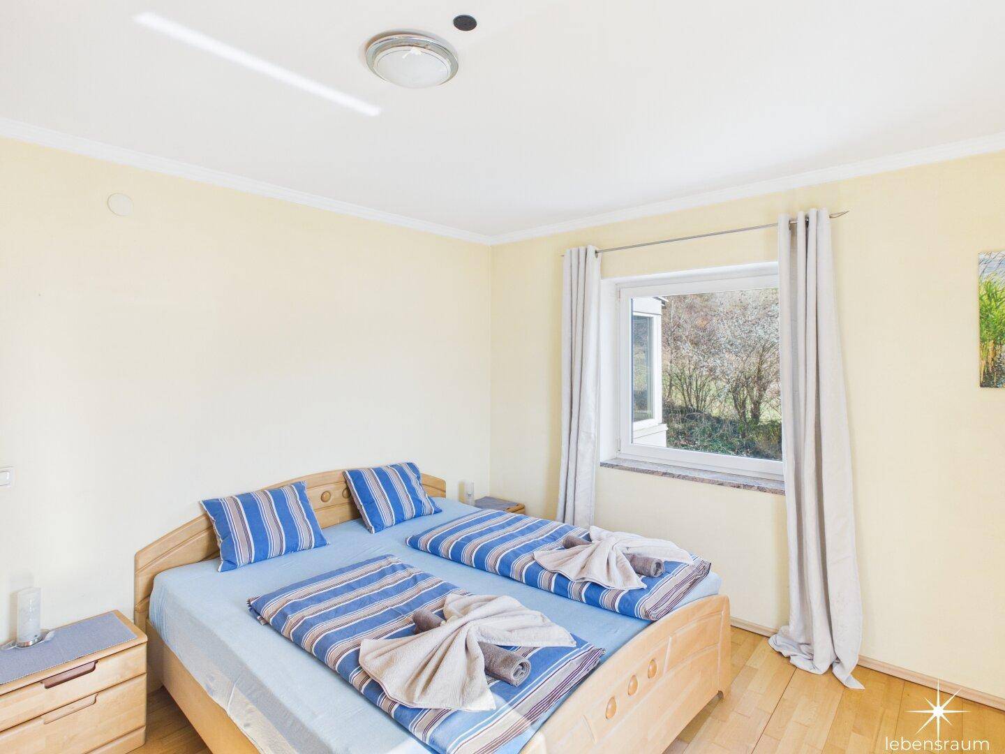 Schlafzimmer mit Holzbett, Parkettboden und Fenster mit Blick ins Grüne.
