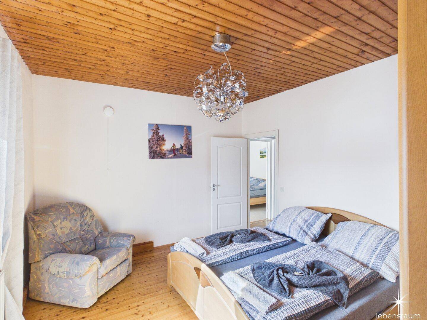 Schlafzimmer mit Holzbalkendecke, Parkettboden und gemütlichem Sessel.