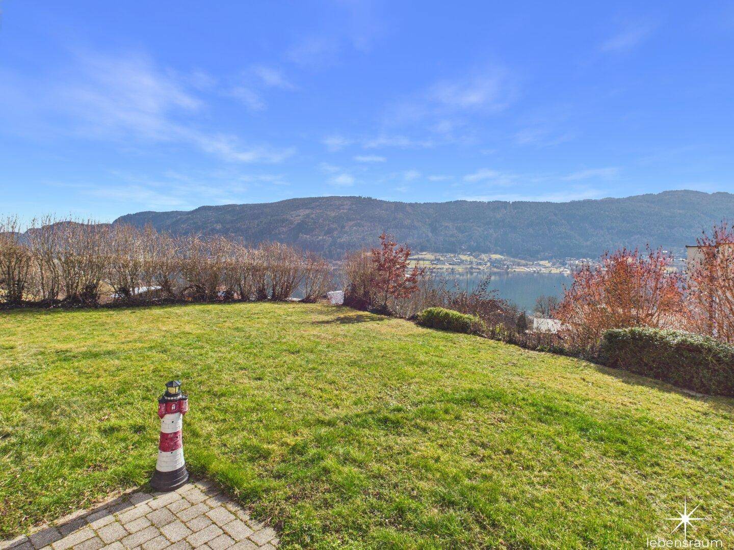 Großer Rasenbereich im Garten mit dekorativem Leuchtturm und weitem Seeblick.