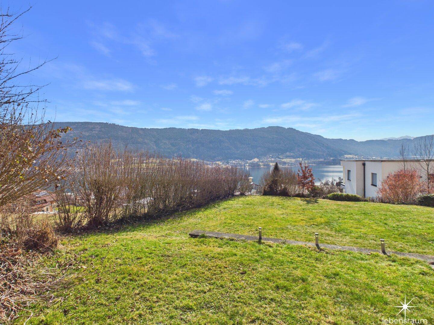 Weitläufiger Garten mit Rasenfläche und Blick auf den See und die umliegende Natur.