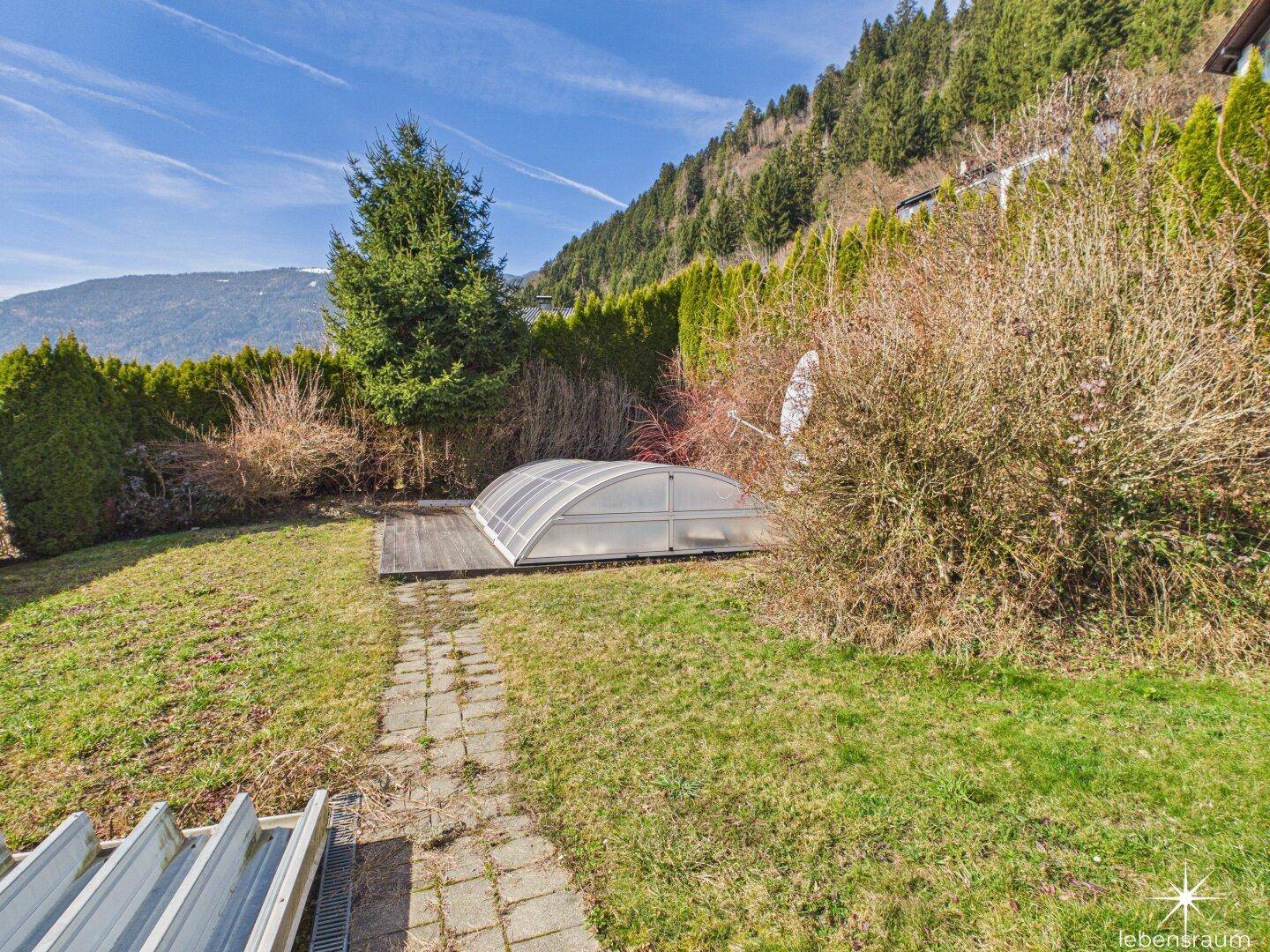 Gartenbereich mit überdachtem Pool, umgeben von Hecken und Bäumen.