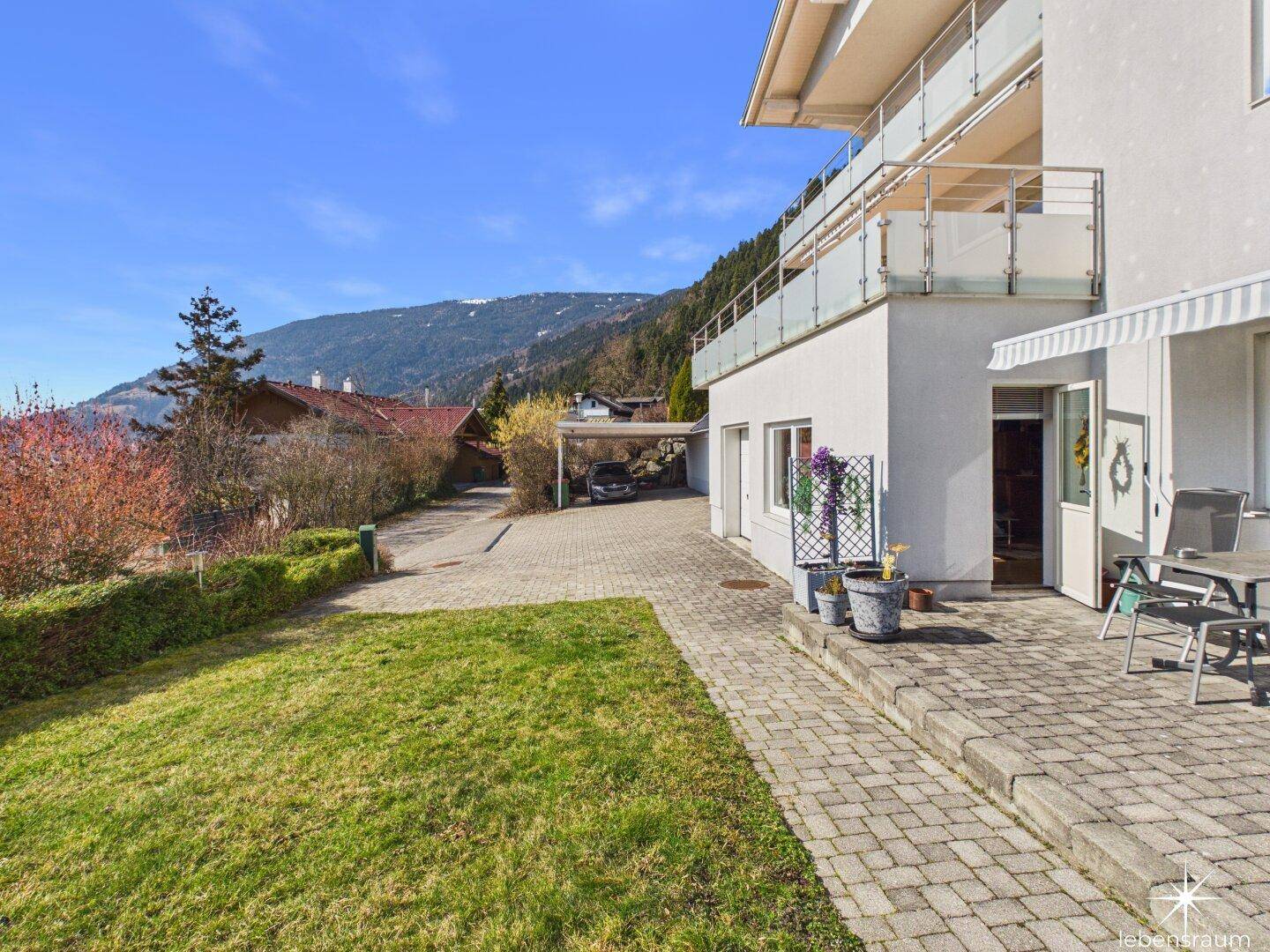 Sonniger Terrassenbereich mit Gartenmöbeln und Zugang zum Rasen mit Bergblick.