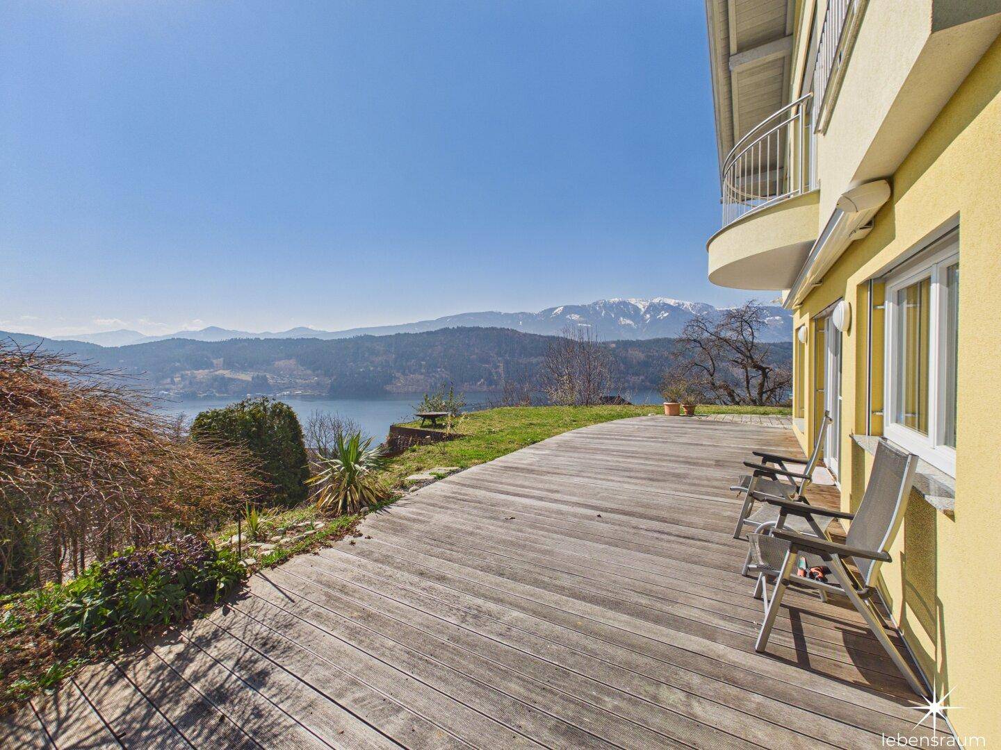 Große Holzterrasse mit Liegestühlen und weitem Blick auf den See und die Berge.