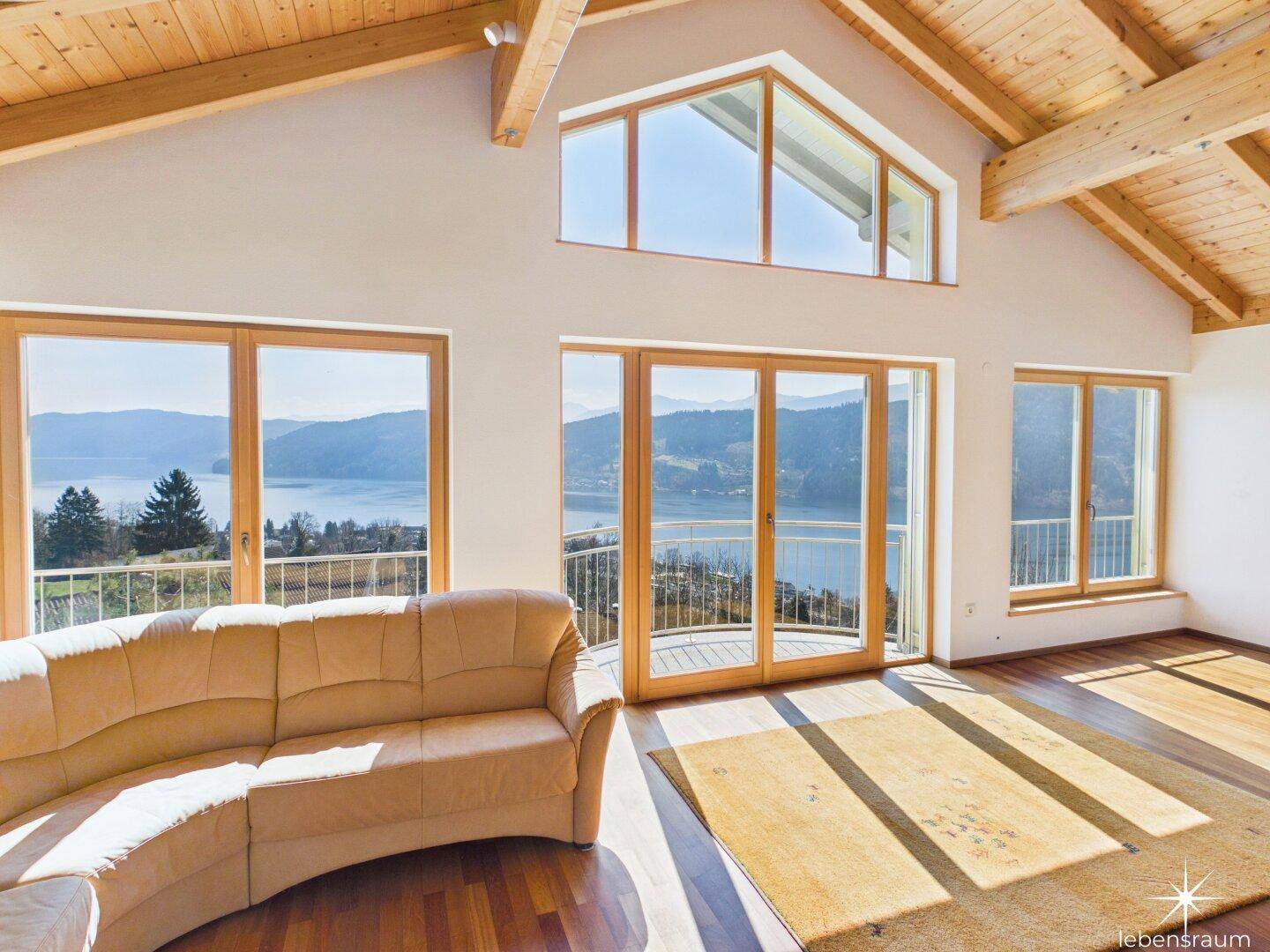 Geräumiges Wohnzimmer mit bequemer Couch, Holzboden und weitem Blick auf den See und die Berge.