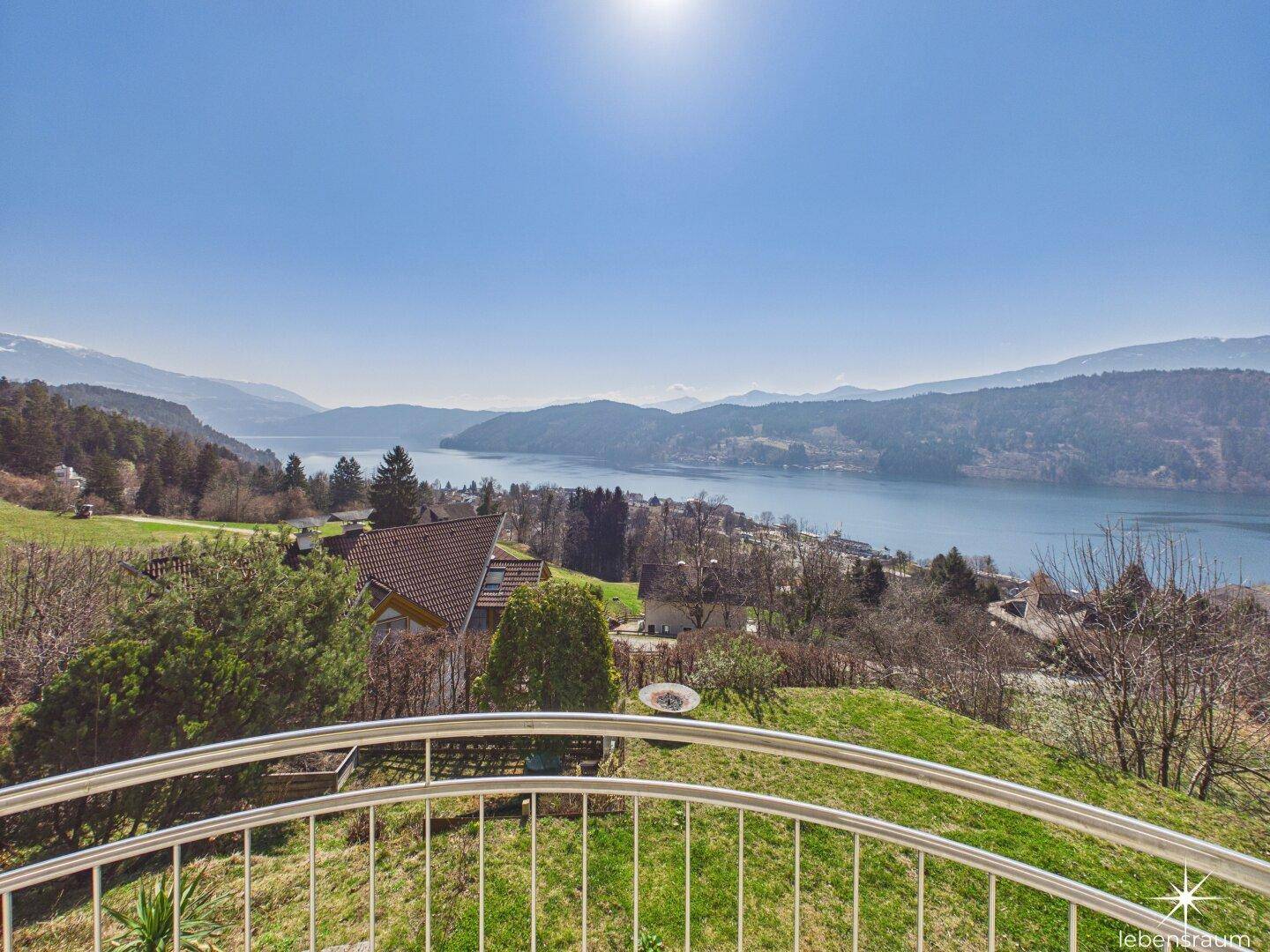 Balkon mit Edelstahlgeländer und weitem Blick über den See und die umliegende Landschaft.