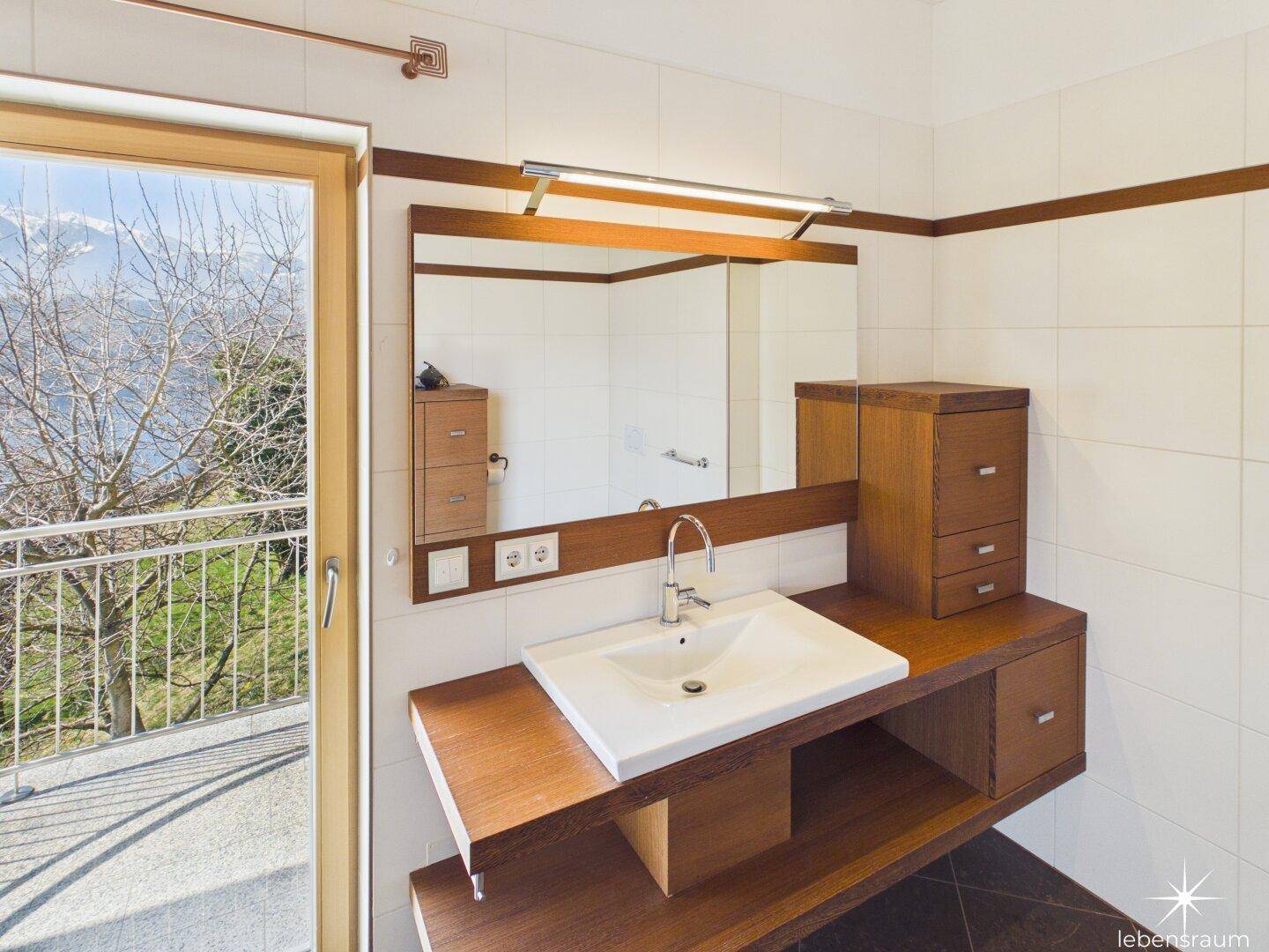 Modernes Badezimmer mit Einzelwaschbecken, Holzmöbeln und Zugang zu einem Balkon mit Aussicht.