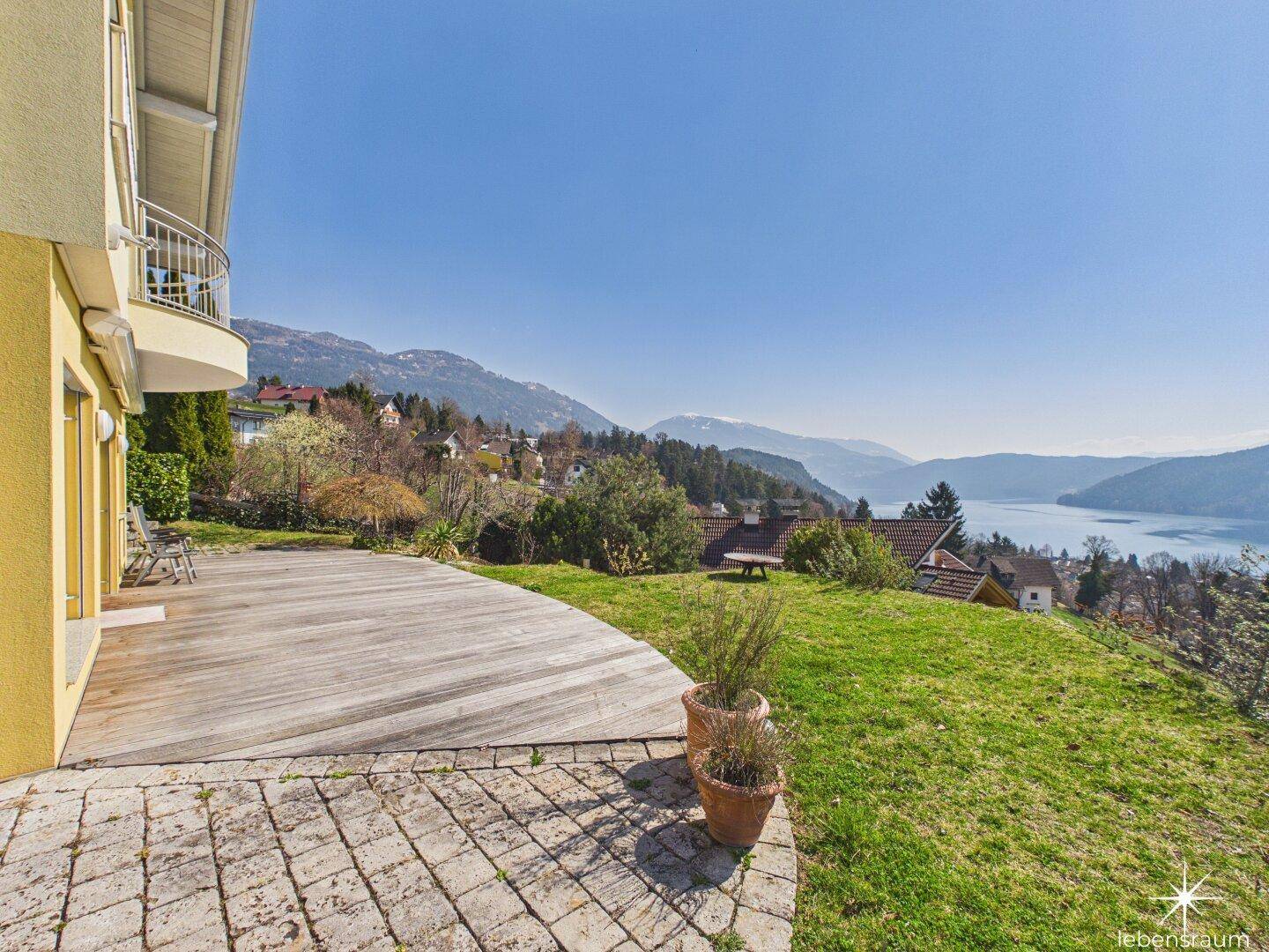 Weitläufige Terrasse mit Holzdeck und Steinplatten, umgeben von Grünflächen und Seeblick.