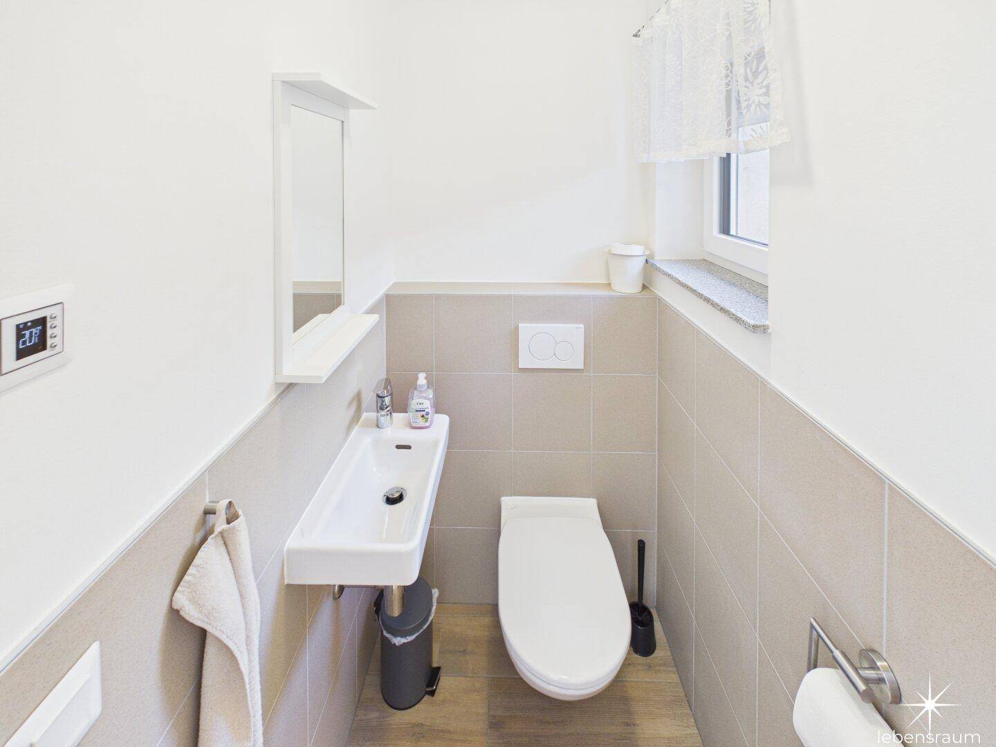 Kleines Gäste-WC mit wandhängendem WC, Waschbecken und Fenster für Belüftung.