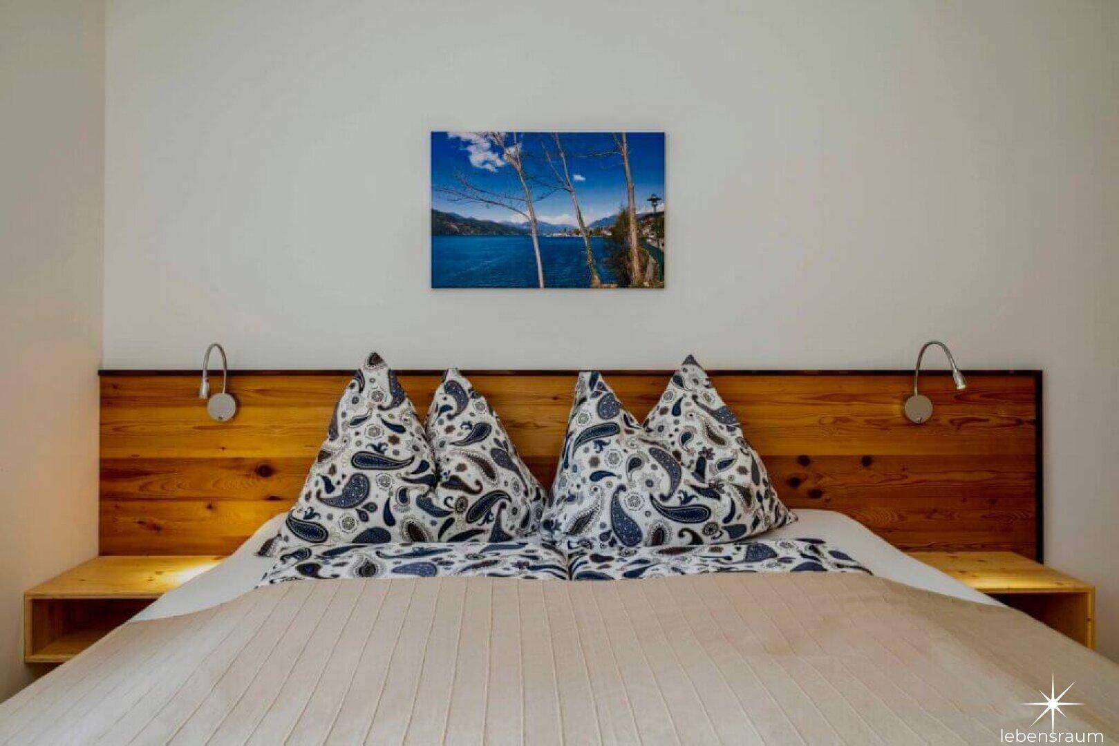 Nahaufnahme des Bettes im Schlafzimmer mit rustikalem Holzkopfteil und Nachttischlampen.
