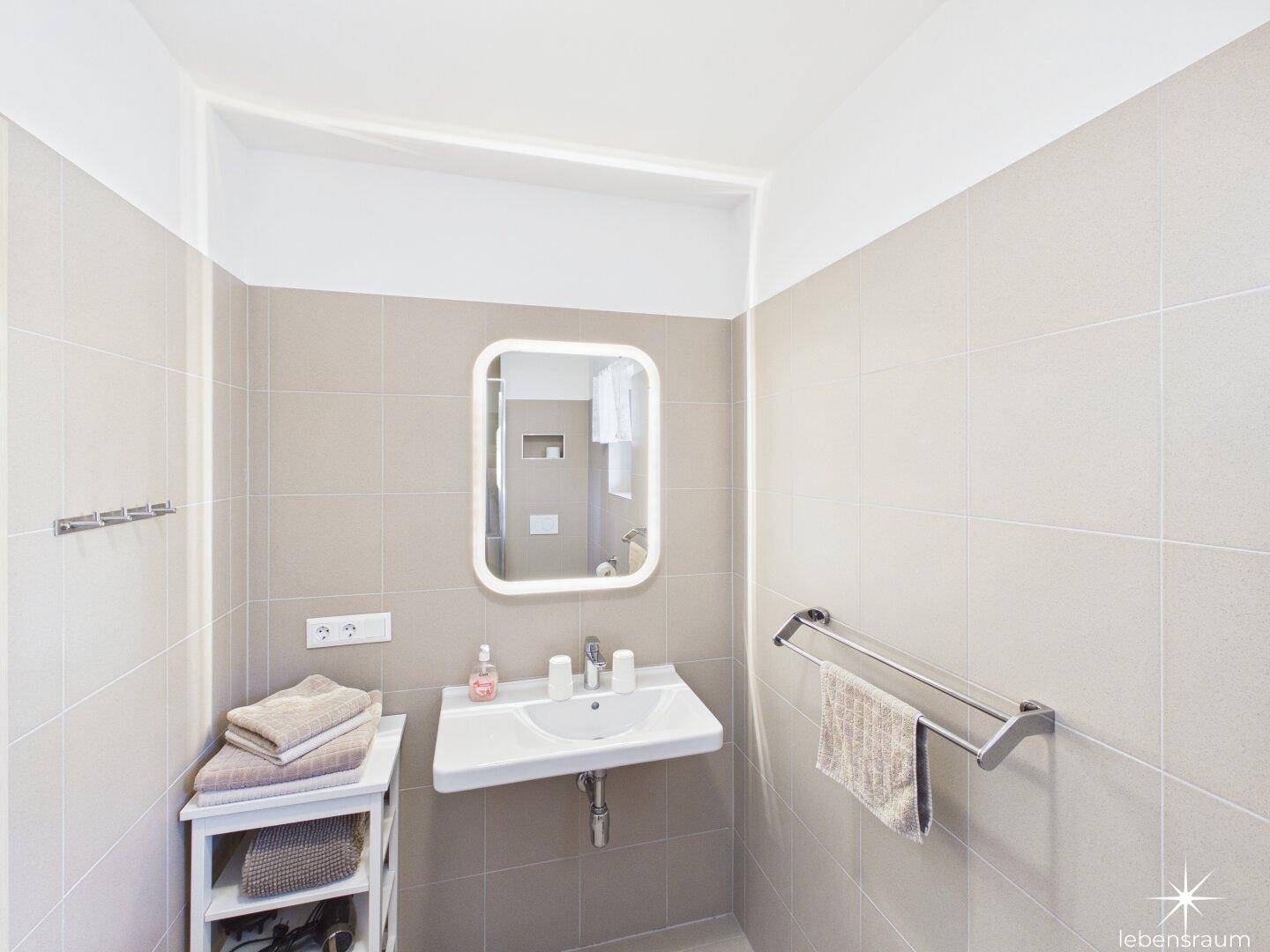 Modernes Badezimmer mit Waschbecken, Spiegel und hellen Fliesen an den Wänden.