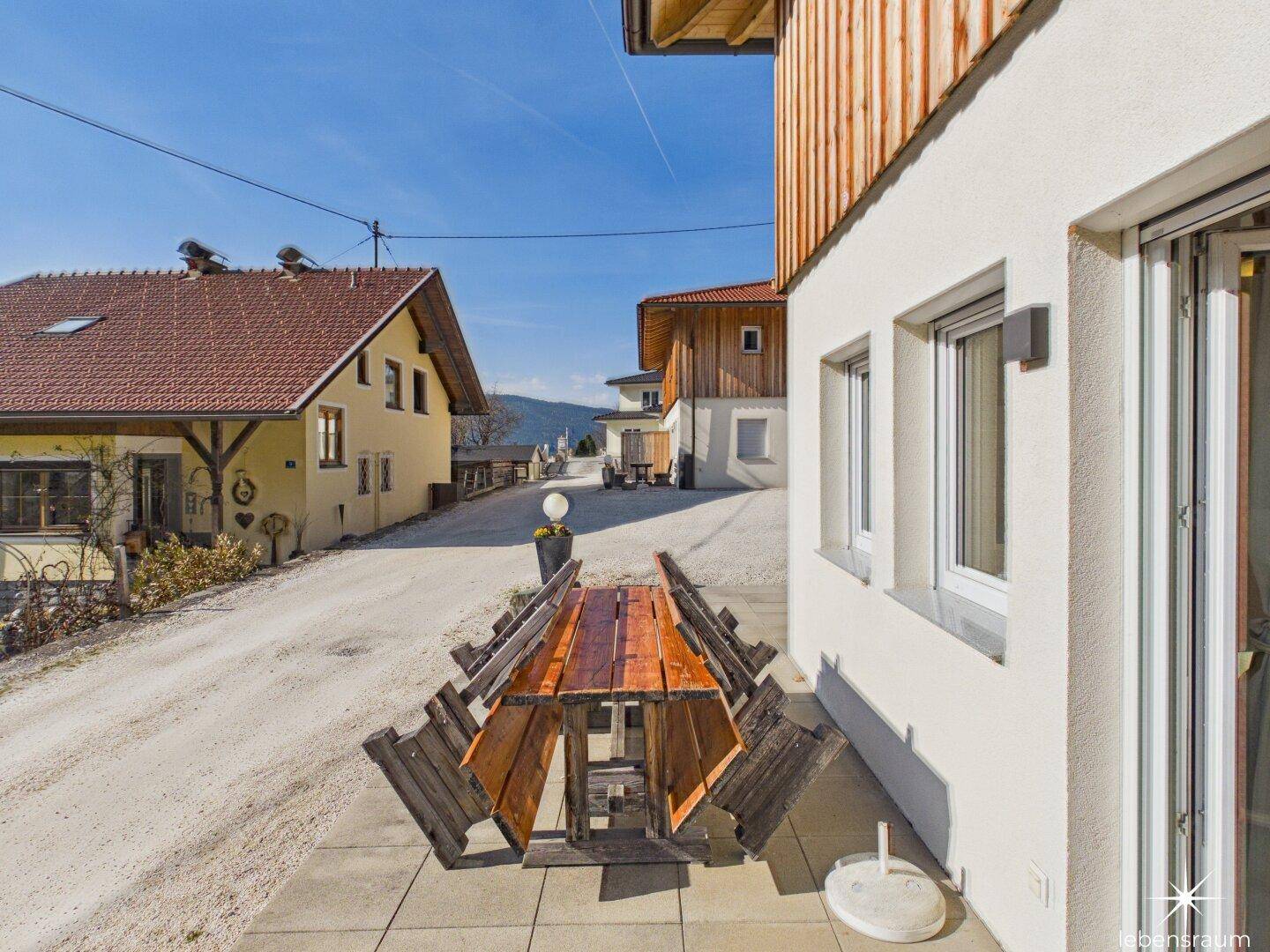 Gepflasterter Außenbereich mit Holztisch und Bänken, ideal für Mahlzeiten im Freien.