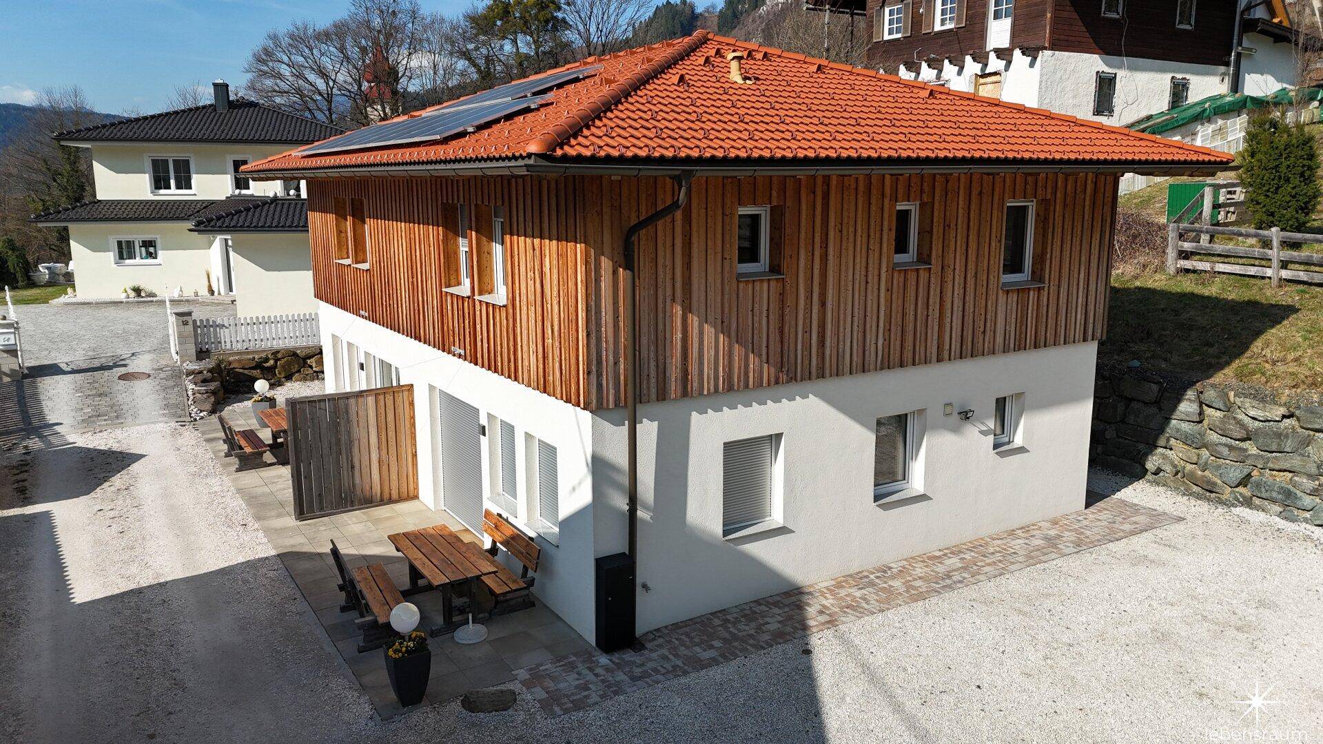 Ansicht des Hauses mit Holzfassade, Ziegeldach und Photovoltaikanlage auf dem Dach.