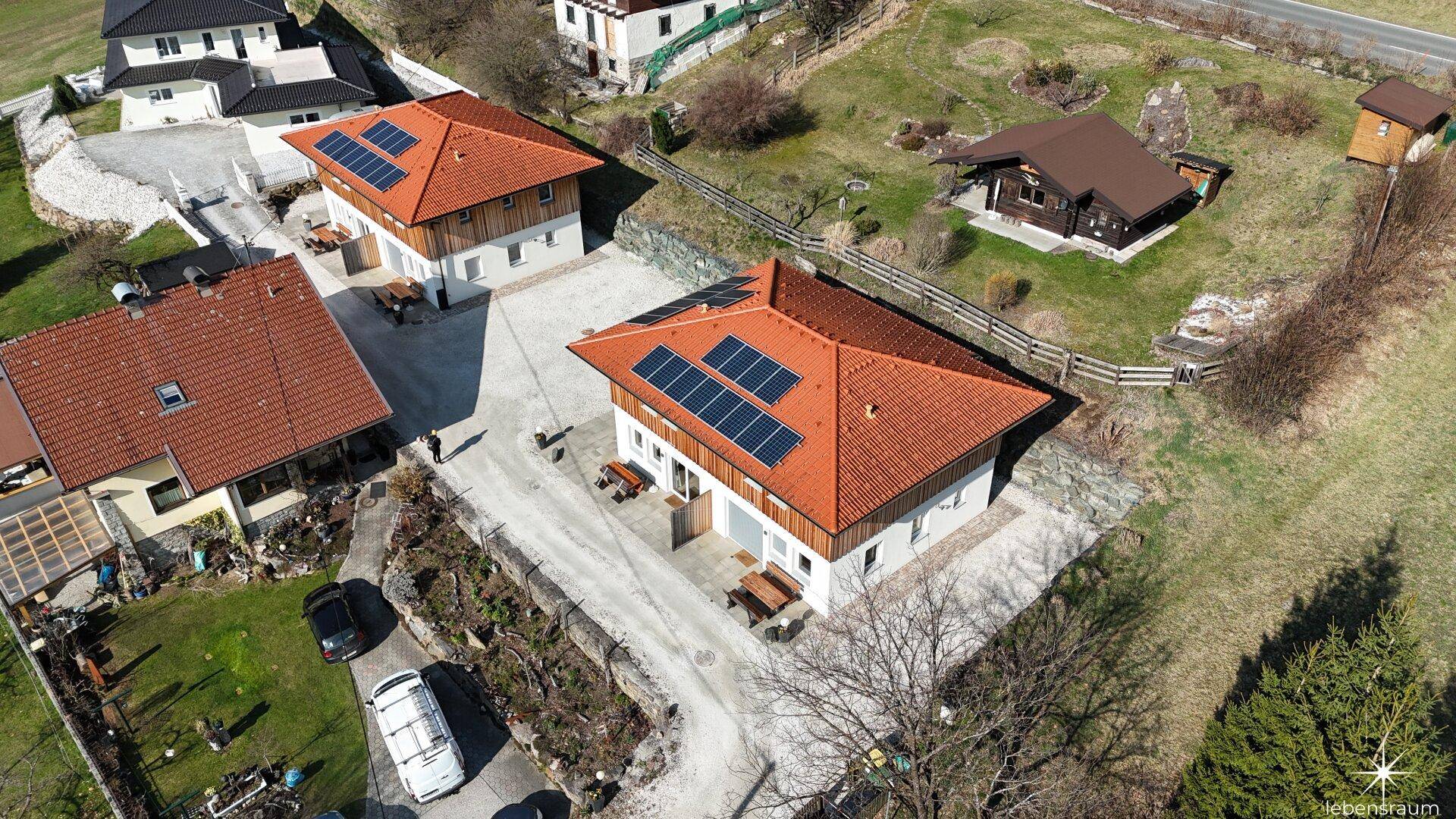 Luftaufnahme einer ländlichen Siedlung mit mehreren Häusern und Photovoltaikanlagen auf den Dächern.