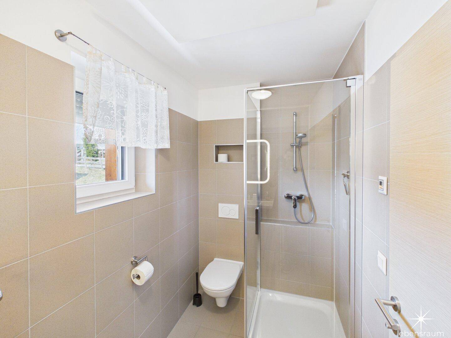 Helles Badezimmer mit Duschkabine, wandhängendem WC und Fenster für Tageslicht.