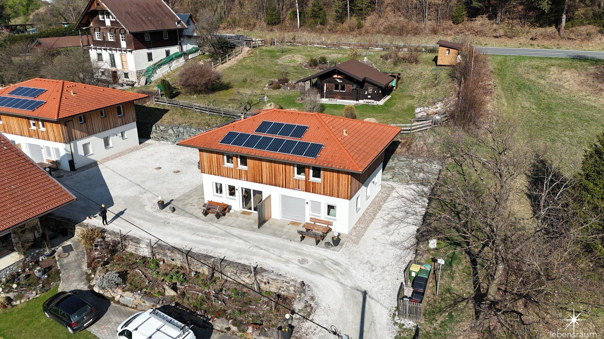 Weitläufige Luftaufnahme der Häuser in einer grünen Umgebung mit Solaranlagen auf den Dächern.